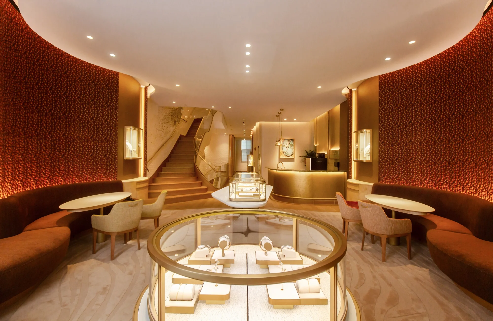 Luxurious jewelry display in a modern hotel lobby with seating areas, decorative walls, a staircase, and warm lighting.