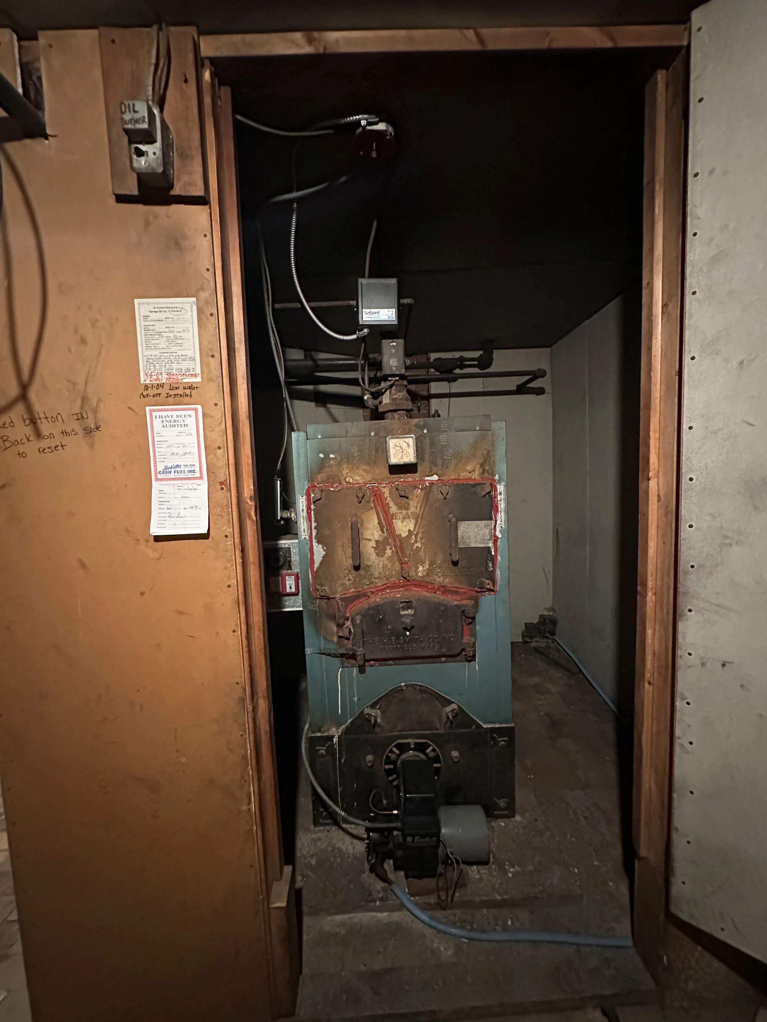Open electrical panel with various wiring and components inside a wooden cabinet.