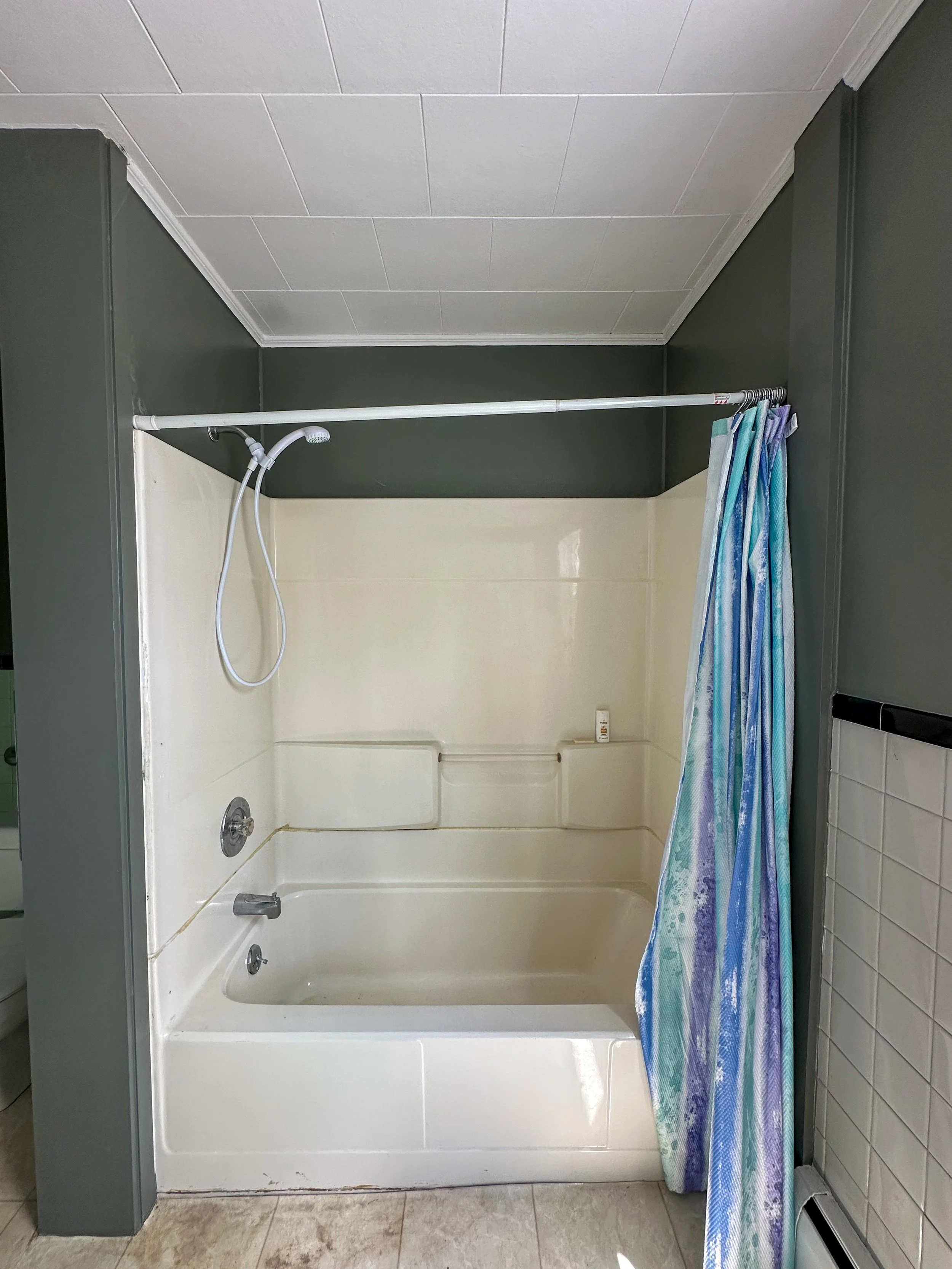Bathroom with white bathtub and shower, gray walls, shower curtain with blue and purple pattern, tiled floor.