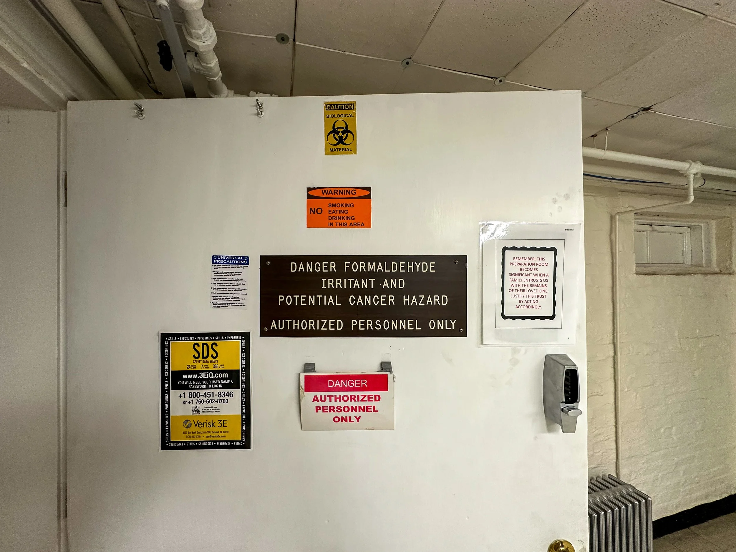 A white wall with multiple safety and warning signs, including symbols indicating biohazard, and text warning of danger, authorized personnel only, and a warning sign for a hazardous substance.