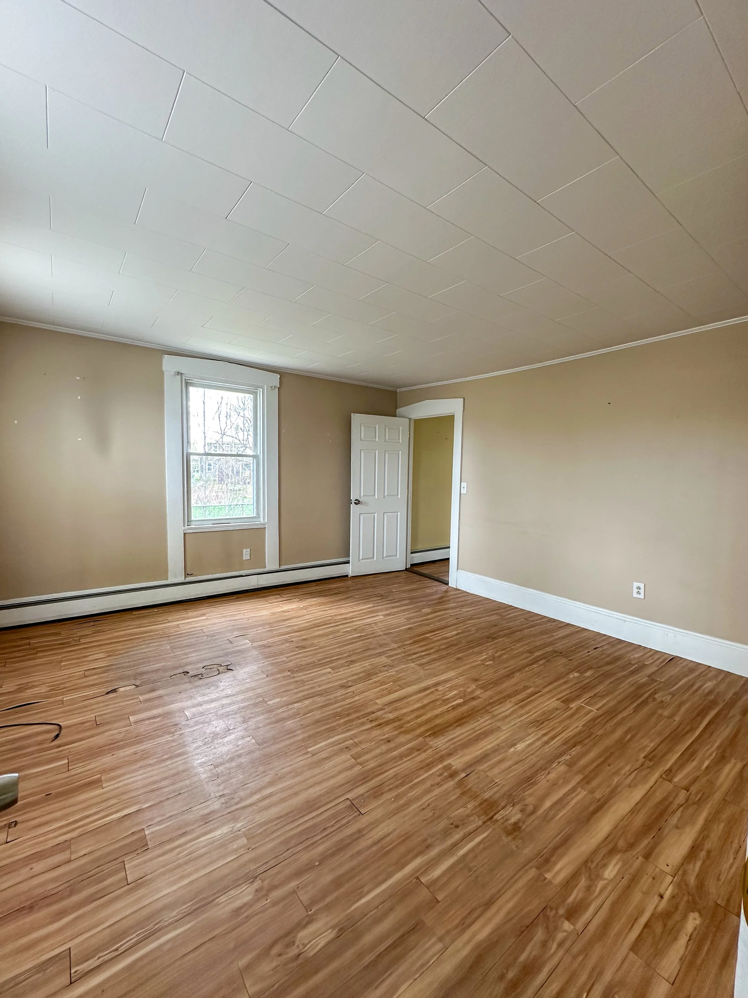Empty room with beige walls, a window, open door, and hardwood flooring.