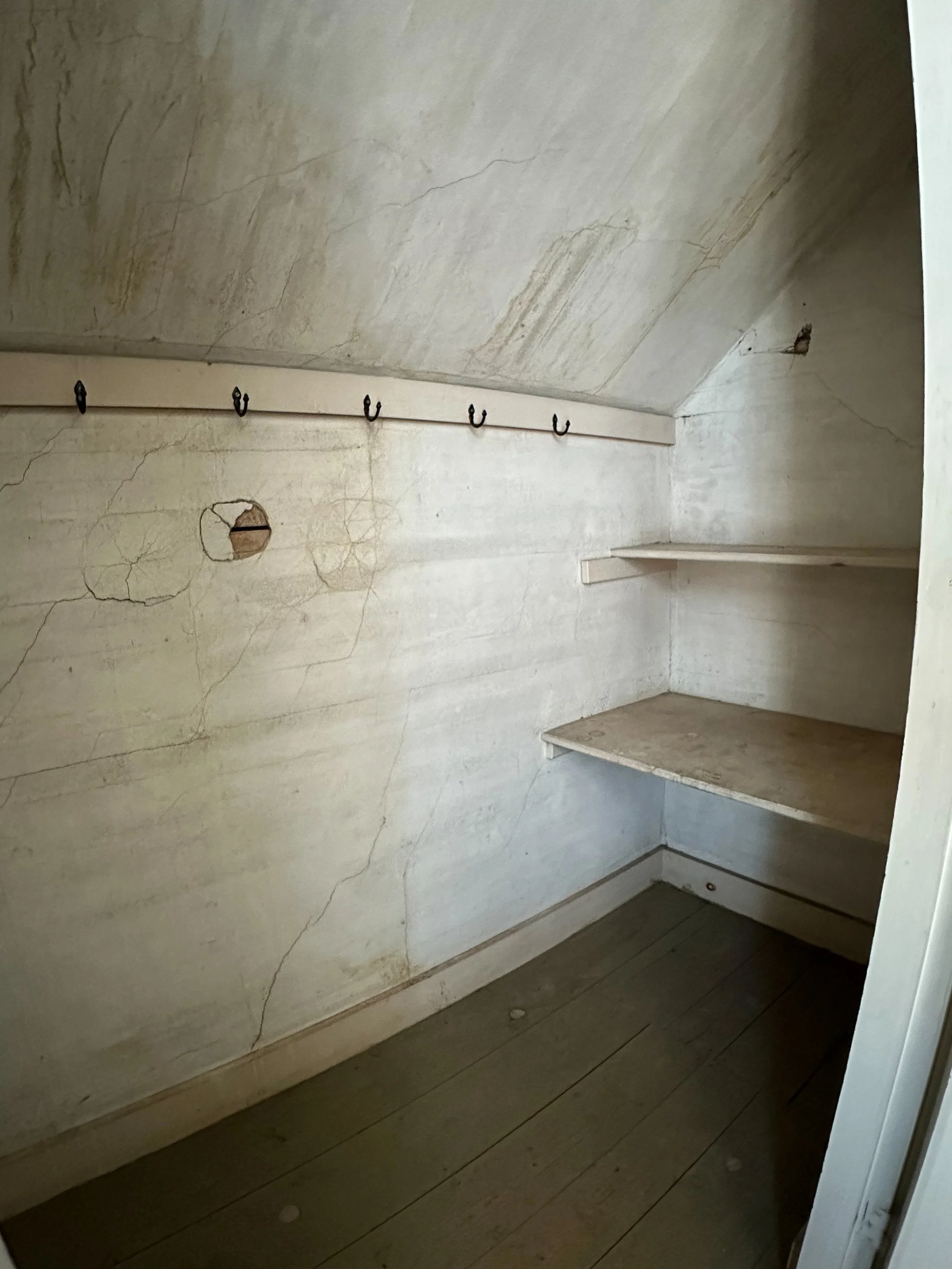 A small, empty walk-in closet with beige marble walls, two floating shelves, and a row of hooks on a strip of wood under the ceiling.