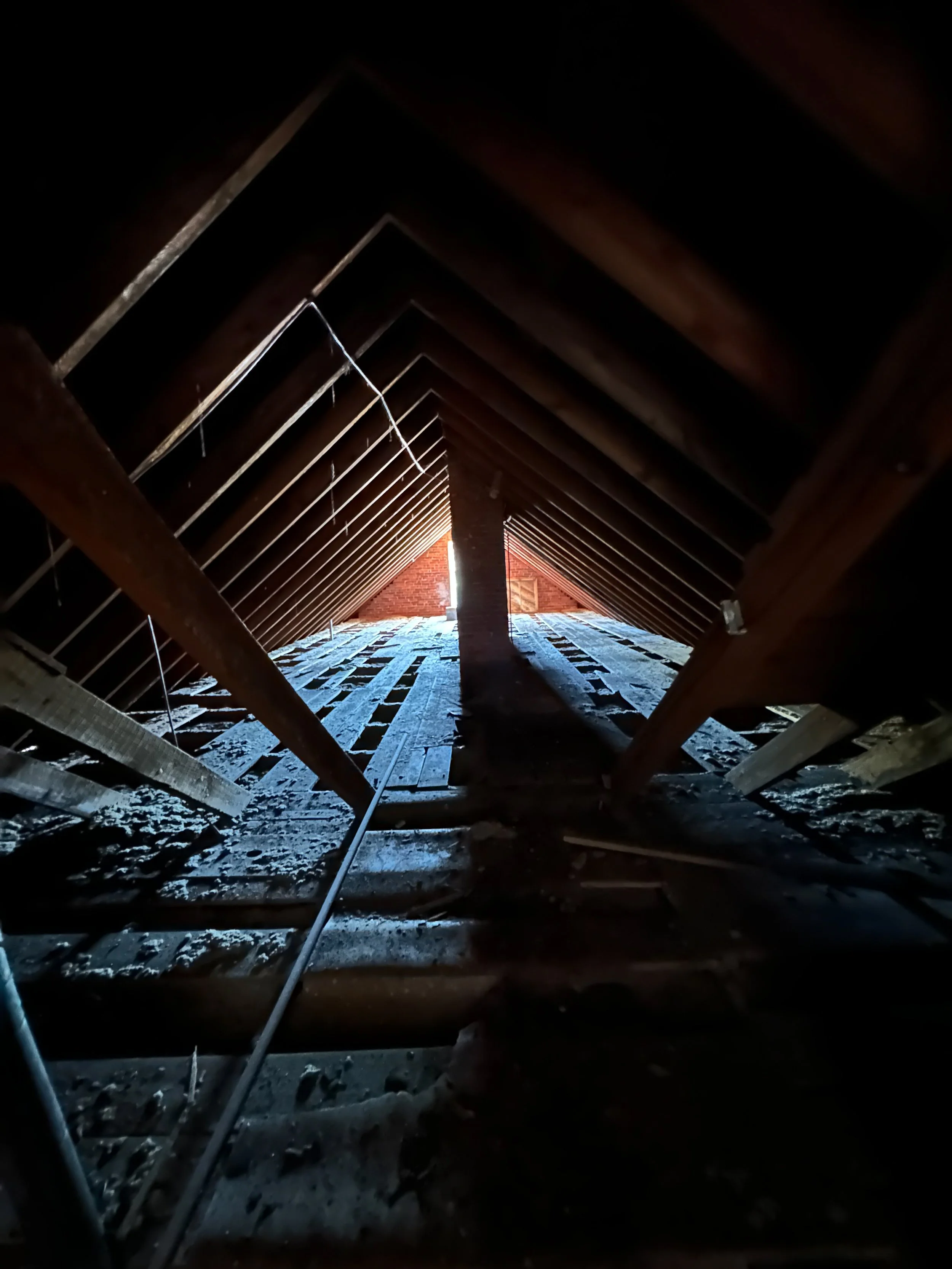 Attic with exposed wooden beams and a brick chimney, with sunlight streaming in from an opening at the end.