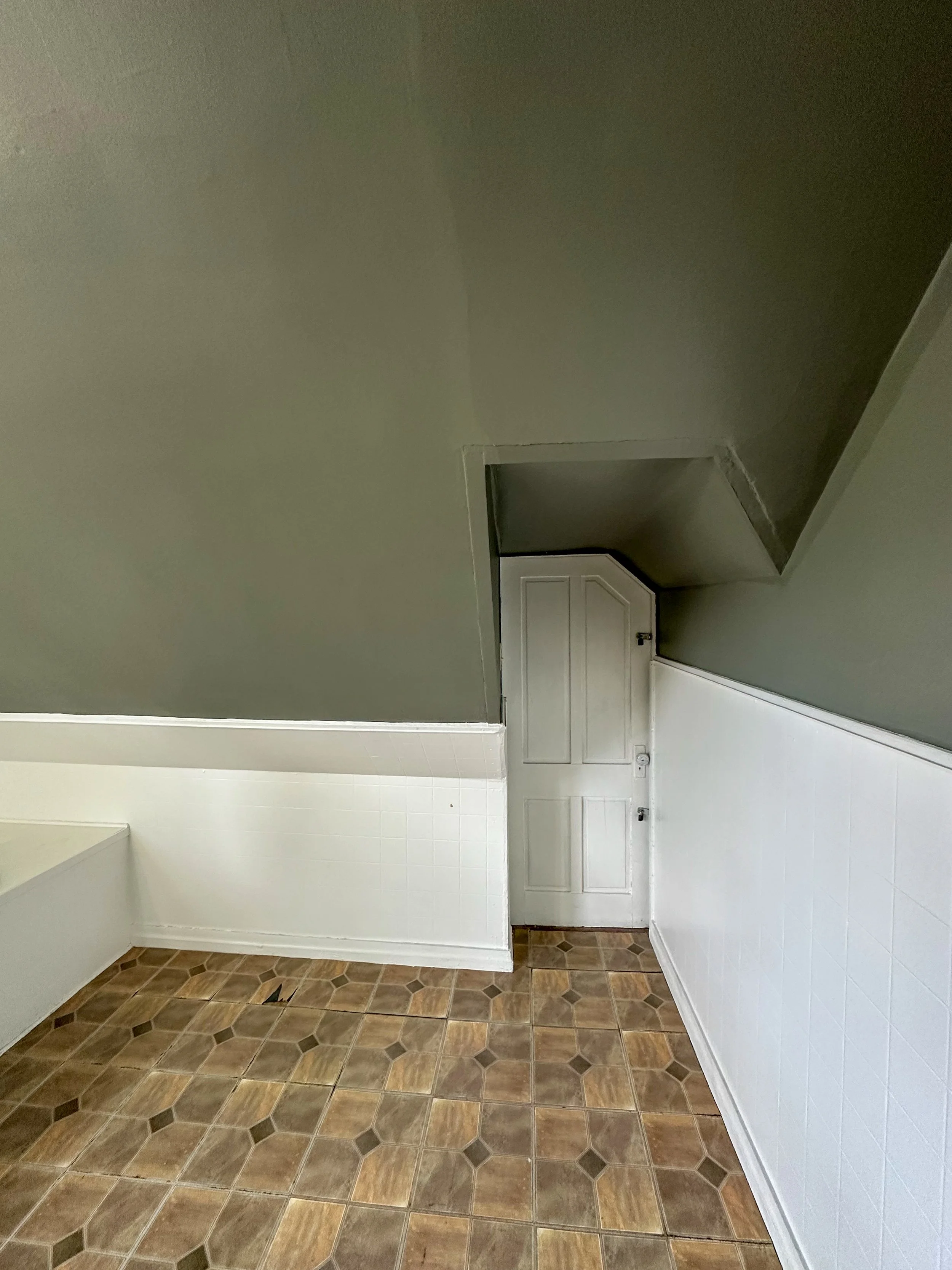 Empty room with hexagonal brown floor tiles, white walls, a white door, and a small open area leading to another space.