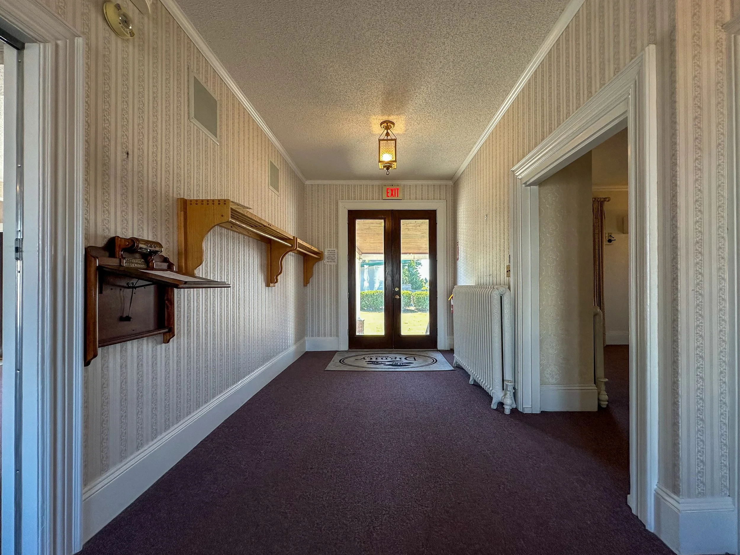 Entrance hallway with patterned wallpaper, wooden shelves, a door with glass panels, and a ceiling light fixture.