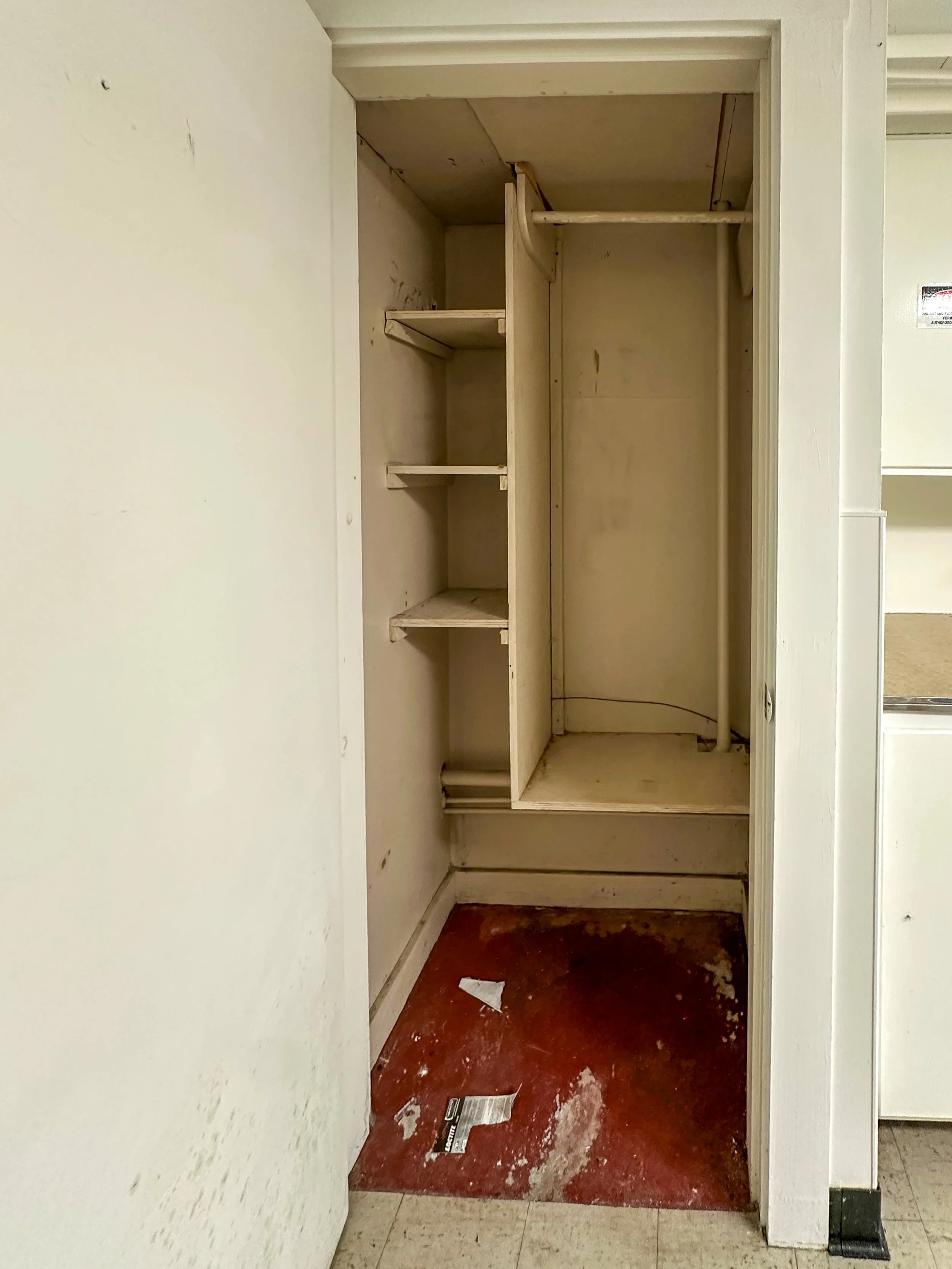Empty closet with open door, shelves on the left side, and a pipe running vertically inside.