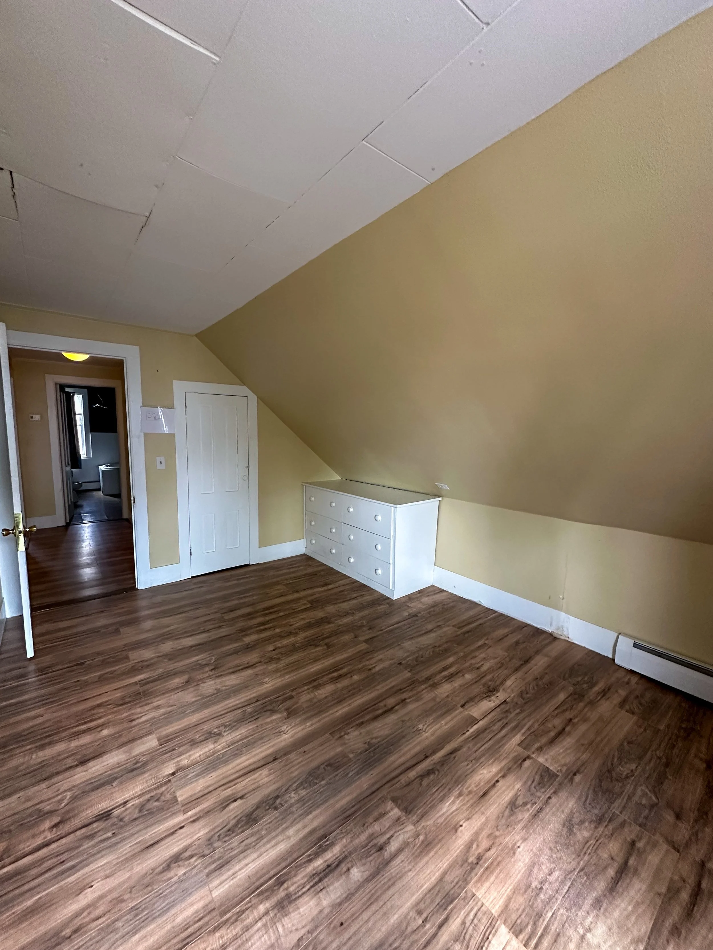 Empty room with yellow walls, a sloped ceiling, hardwood floor, a white dresser, and two doorways.