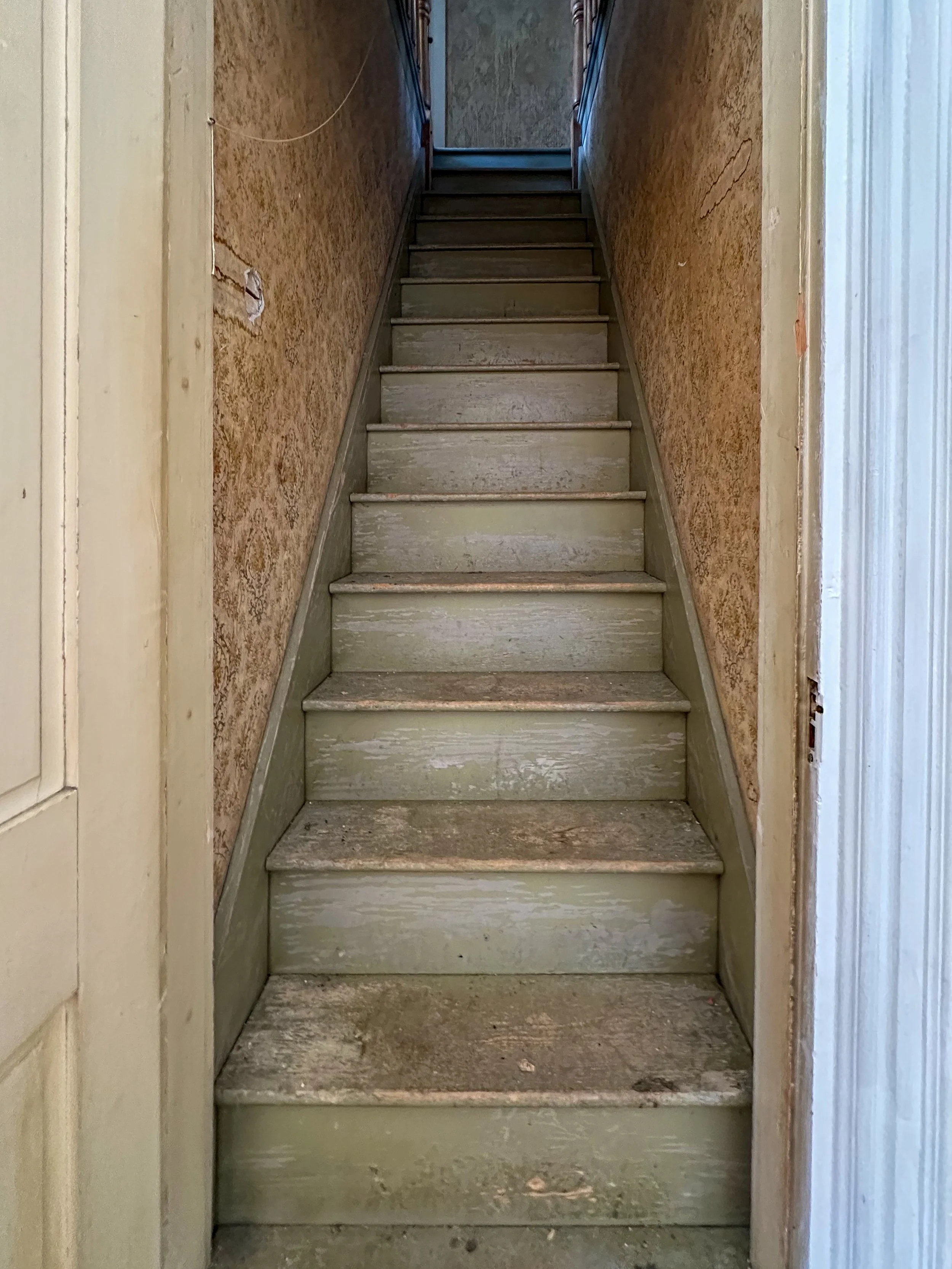 Old, weathered wooden stairs leading up to a door at the top, with worn walls on either side.