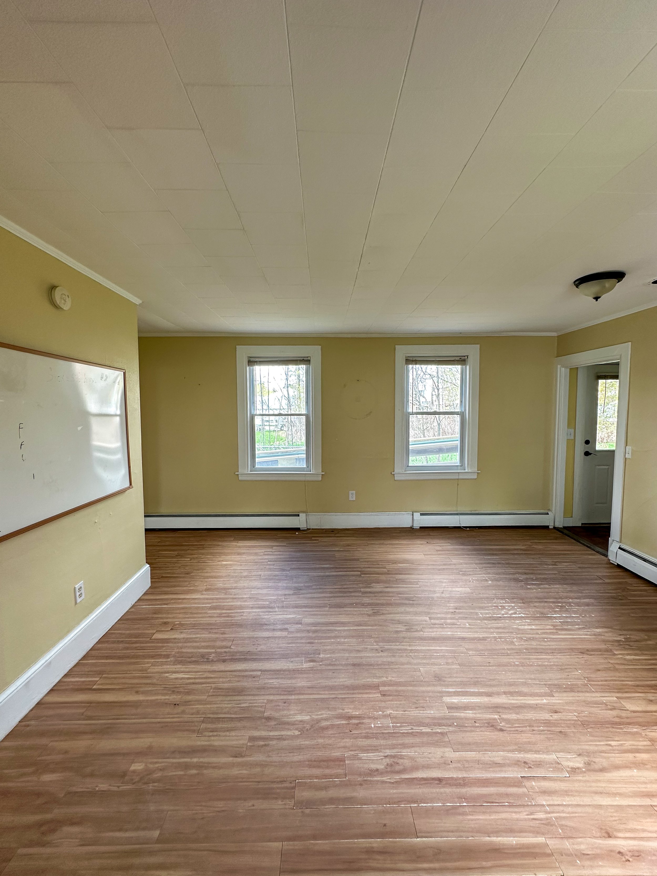 Empty room with yellow walls, hardwood flooring, three windows, and white trim, with ceiling light fixtures.