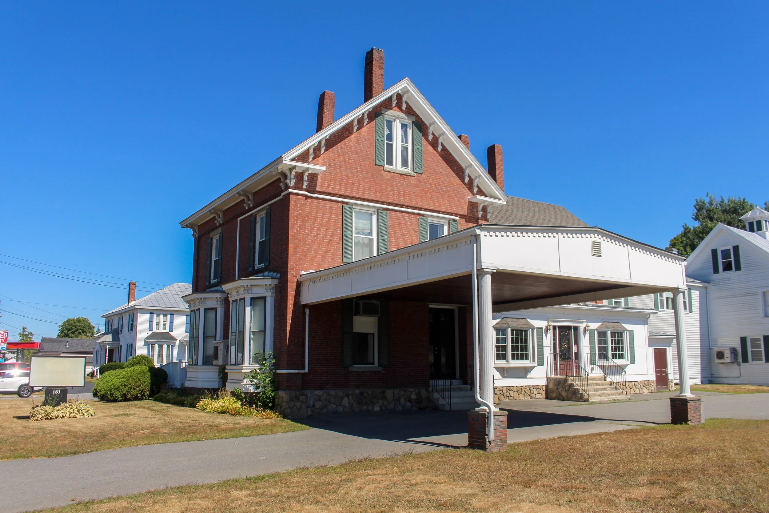 A red brick house with a white porch and green shutters under a clear blue sky.