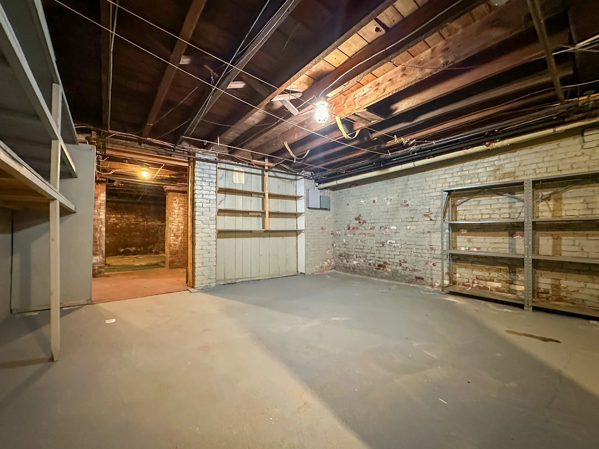 Empty garage with wood and brick walls, shelving units, and exposed ceiling beams.
