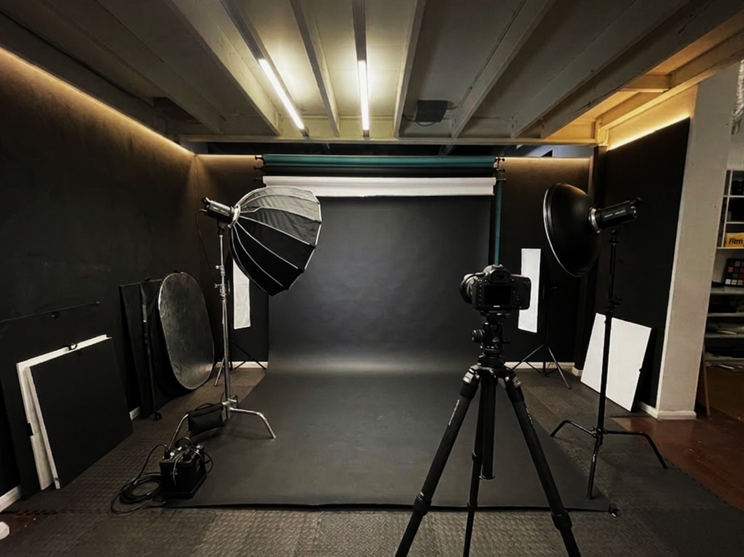 Photography studio setup with a gray backdrop, professional lighting, camera on tripod, and various reflectors and panels.