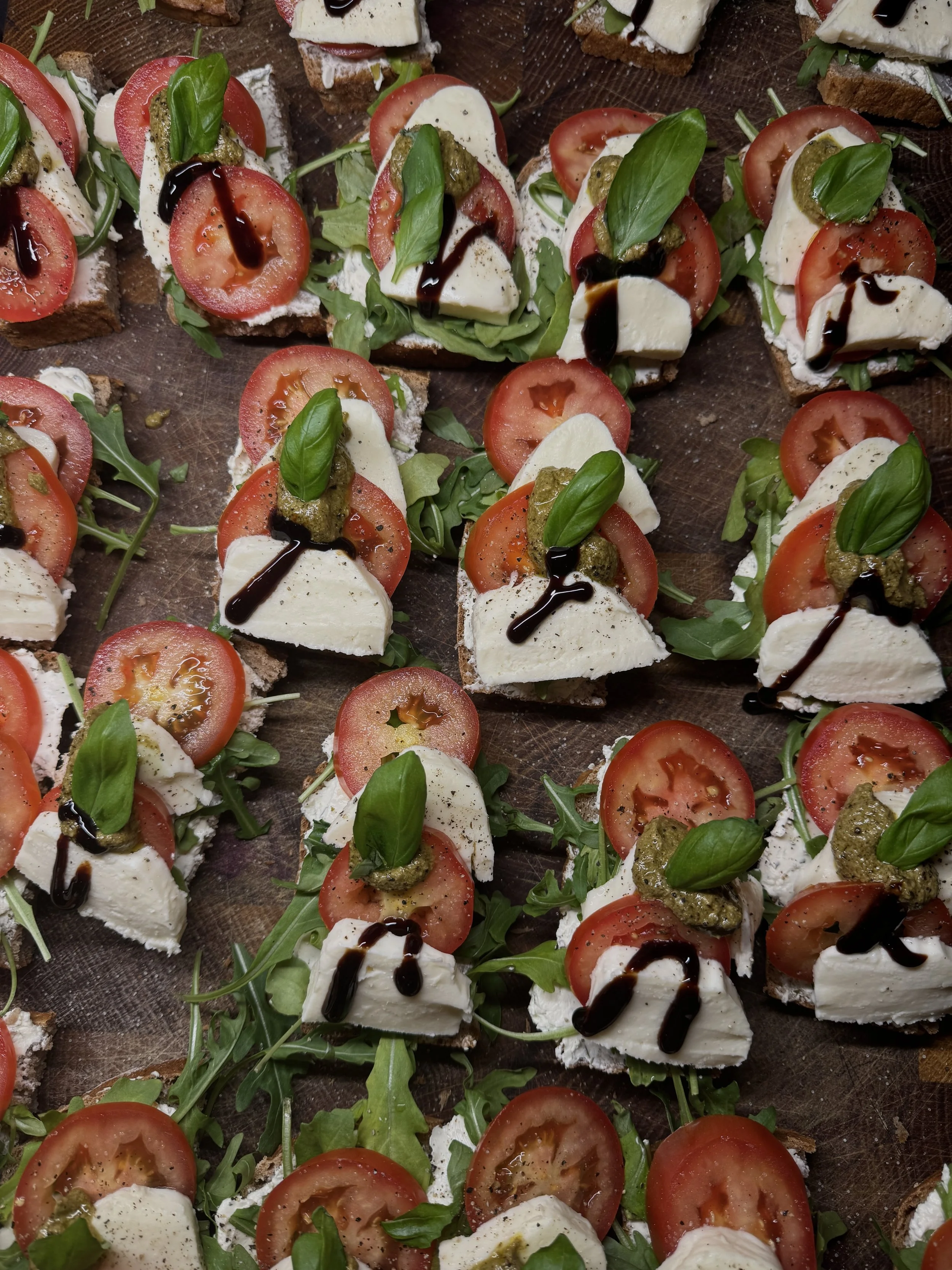 Verschiedene belegte Brotscheiben mit Tomate, Mozzarella, Basilikum, Pesto, Rucola und Balsamico-Reduktion.