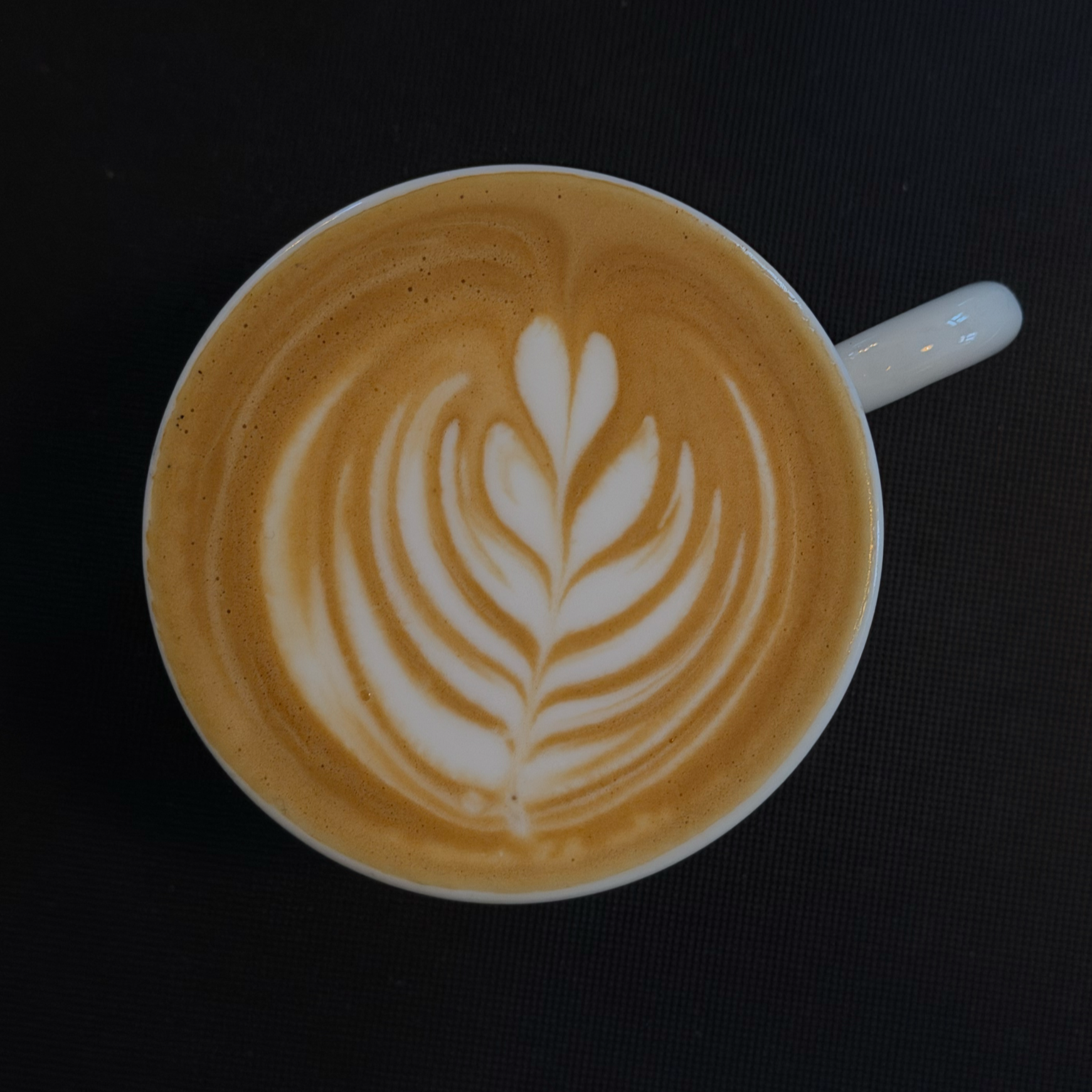 Eine Tasse Kaffee mit Milchschaumkunst im Herz-Design auf schwarzem Hintergrund.