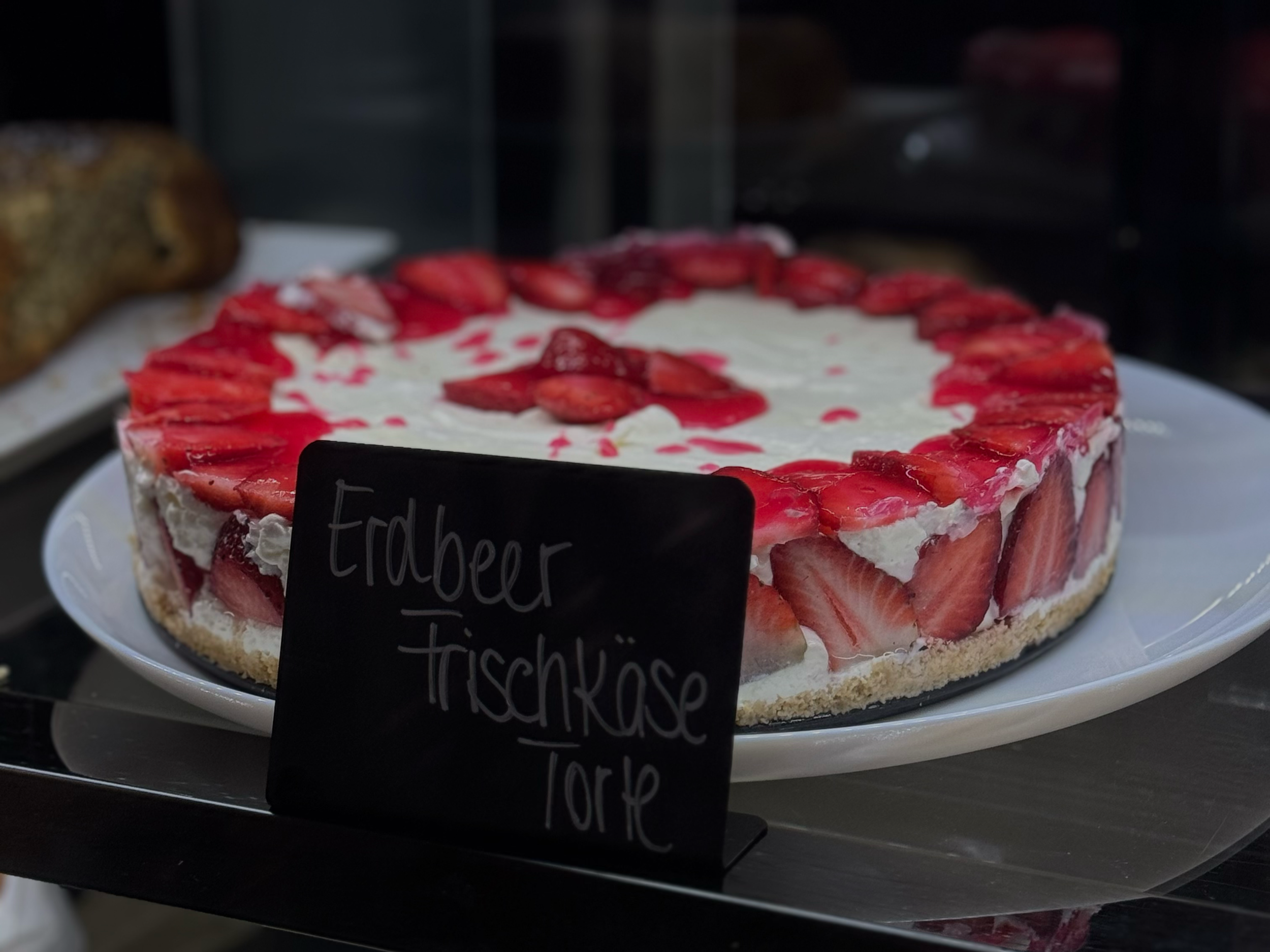 Kuchen mit Erdbeeren und Sahne, auf einem Teller, mit Handgeschriebener Beschriftung "Erdbeerkuchen" in der Nähe