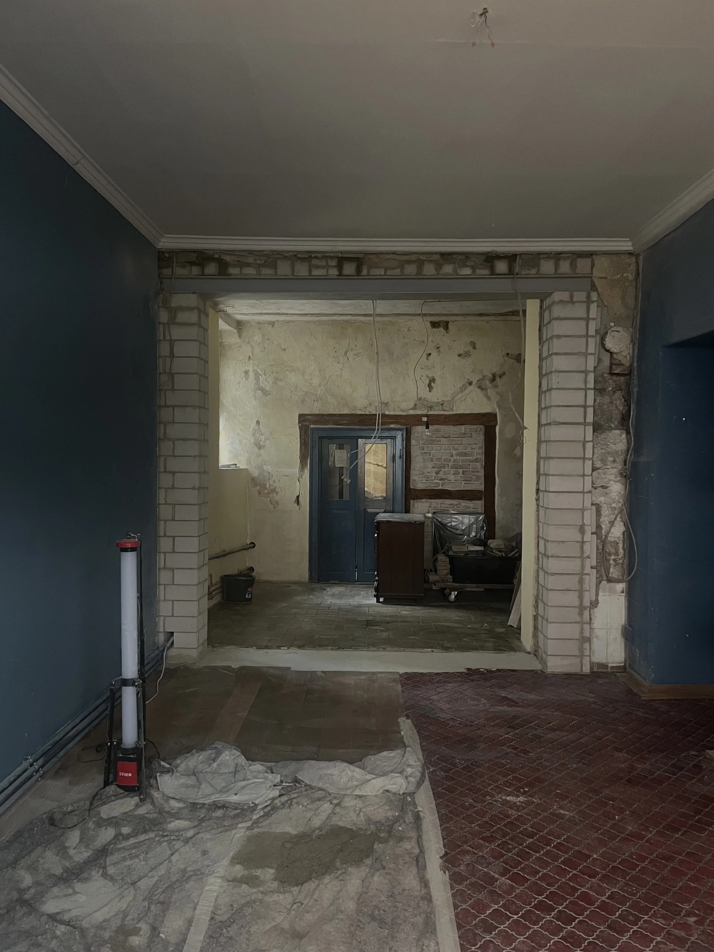 Innenraum einer Baustelle mit unvollständiger Wand- und Raumdekoration. Es gibt eine blaue Wand, einen  Ziegelrahmen, eine Tür und verschiedene Baumaterialien auf dem Boden.