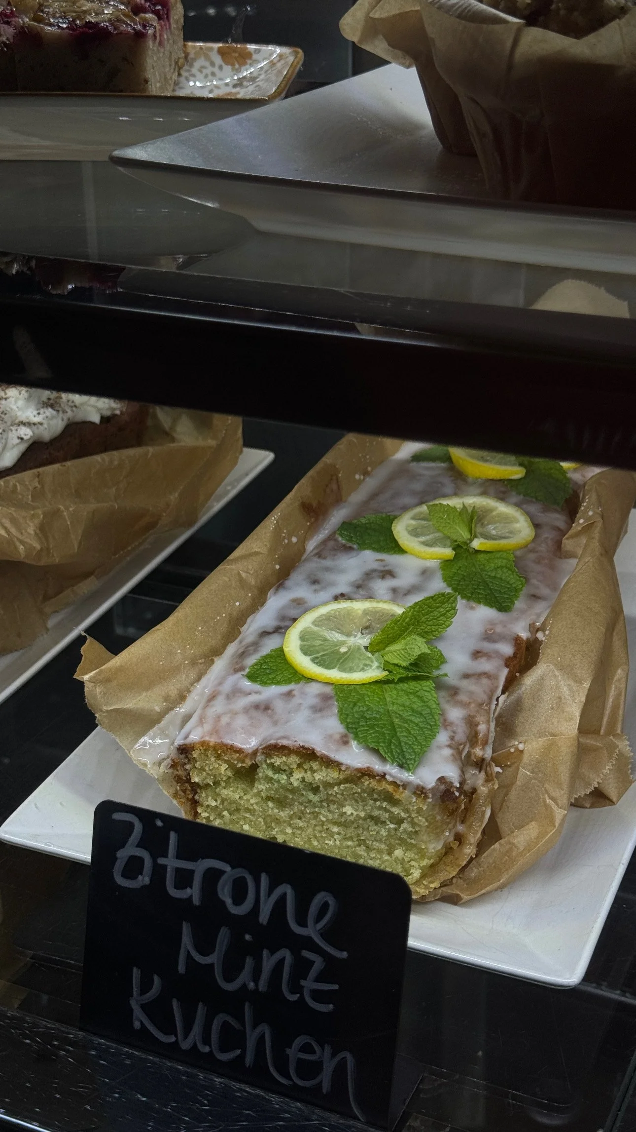 Ein Zitronen-Kuchen mit Glasur, Gartenschaum, Zitronenscheiben und Minzblättern auf einem weißen Teller.
