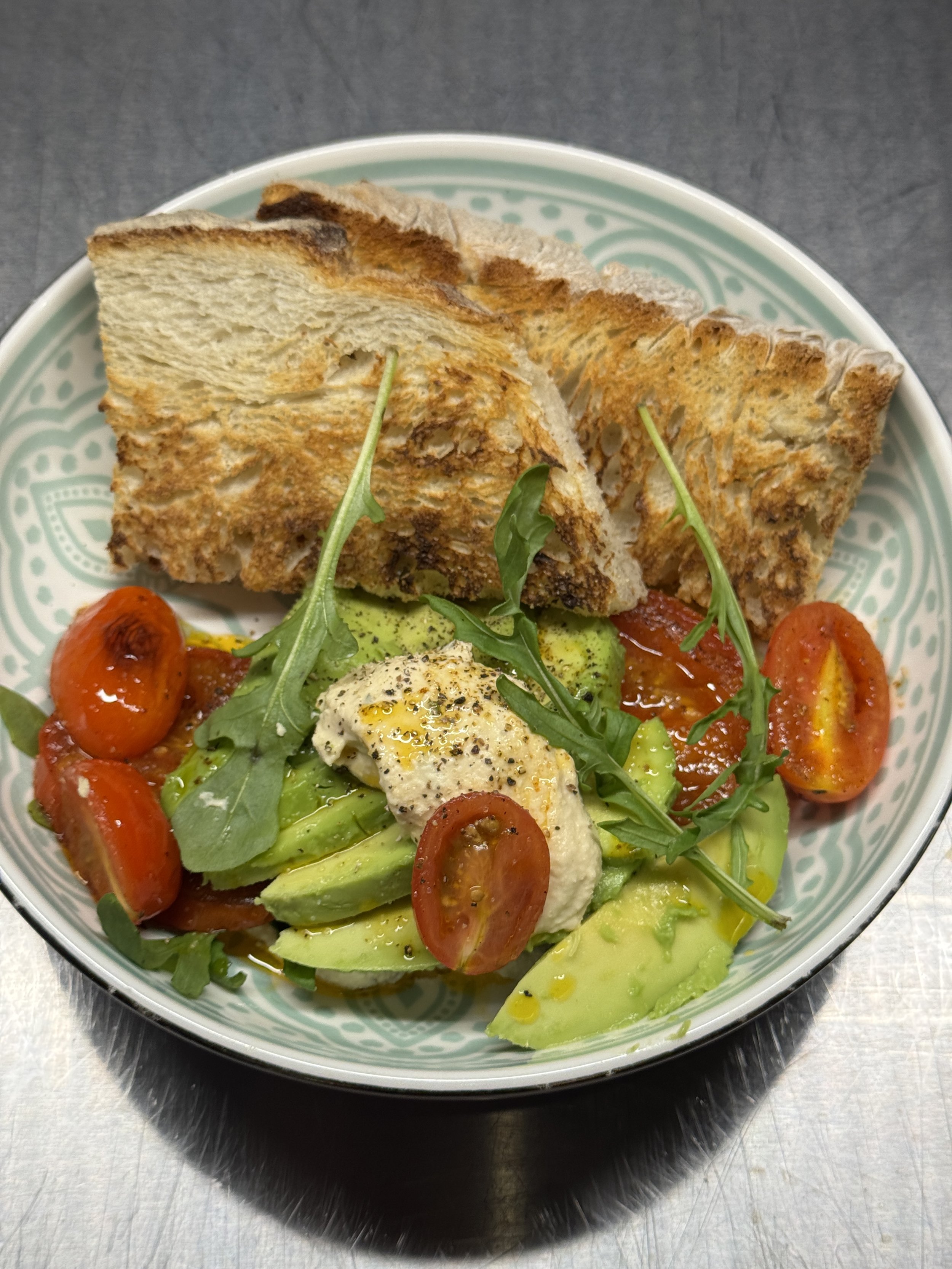 Blick auf einen bunten Salat mit Tomaten, Avocado, Rucola, einem pochierten Ei und geröstetem Brot in einer Schüssel.