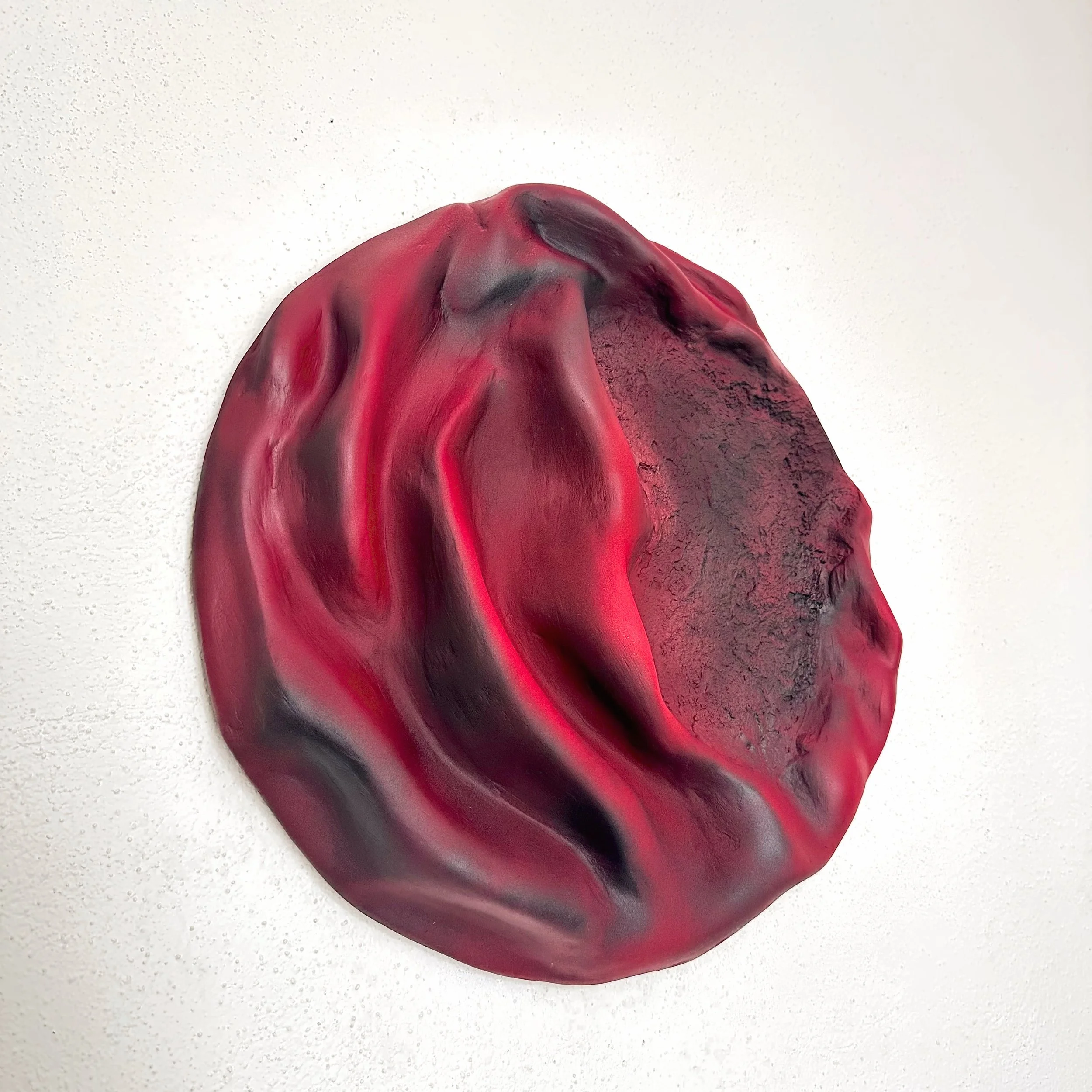 Close-up of a red and black abstract sculpture or object against a white background.