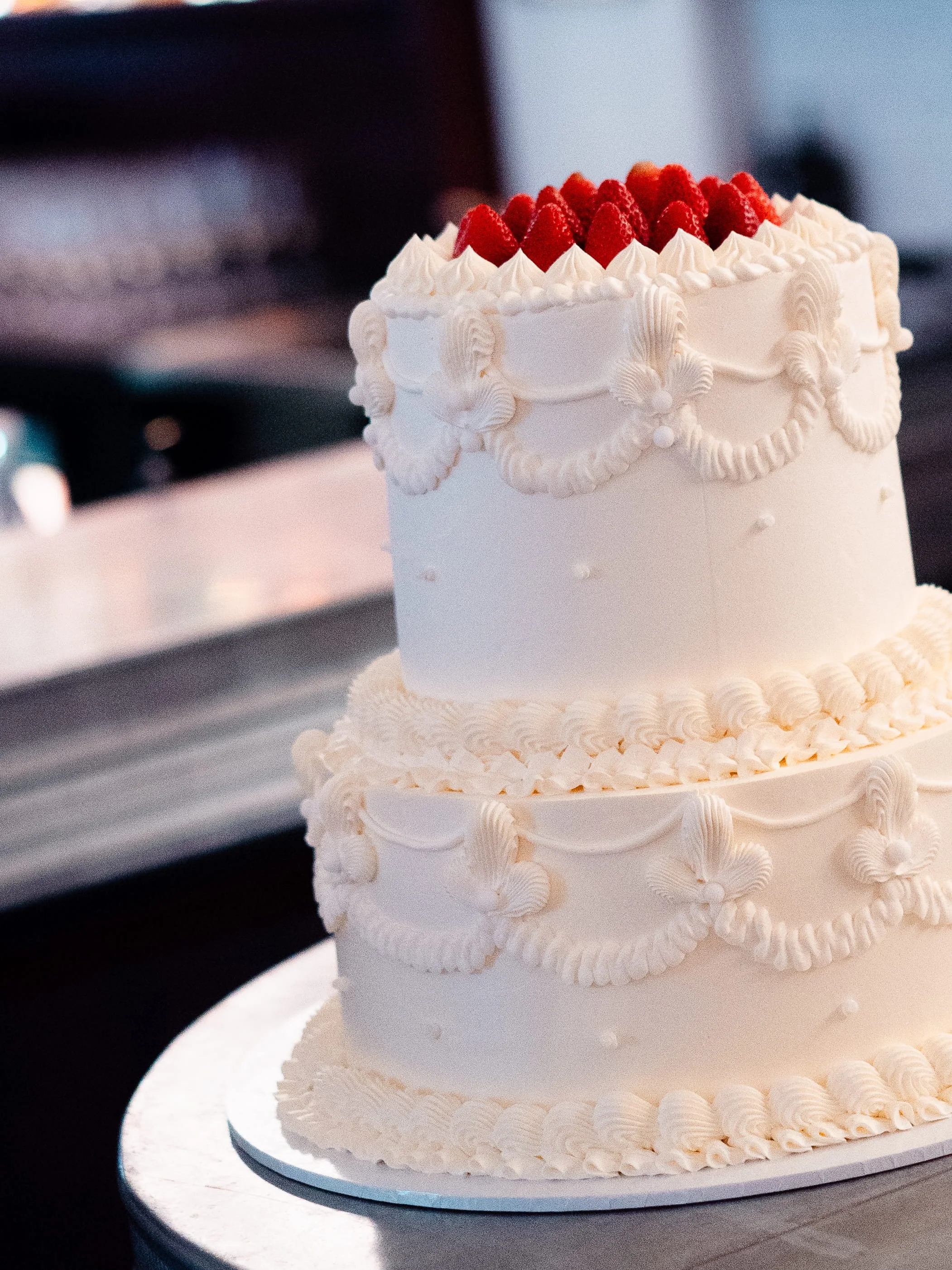 A white cake decorated with piped cream and strawberries on top.