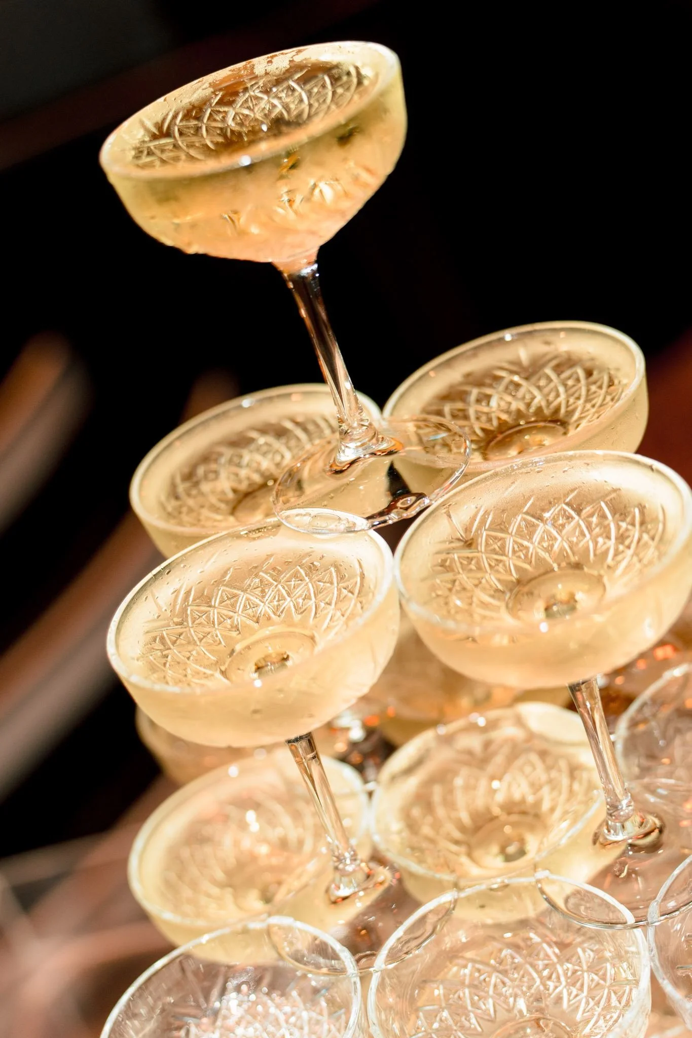 Stacked champagne glasses with intricate etched patterns on the bowls, set against a dark background.