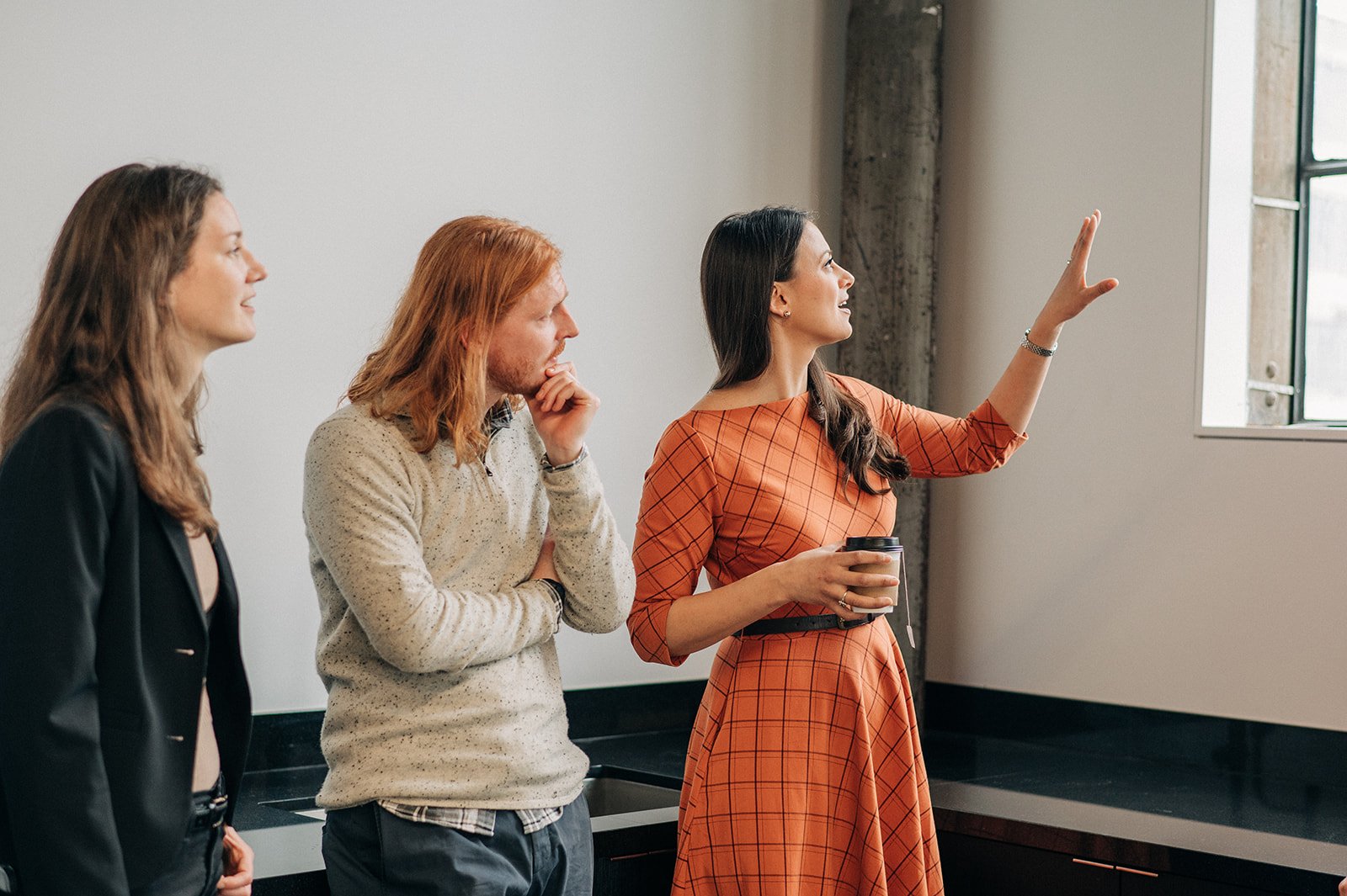 Four women standing near a window, one woman pointing at the window while holding a coffee cup, others looking on