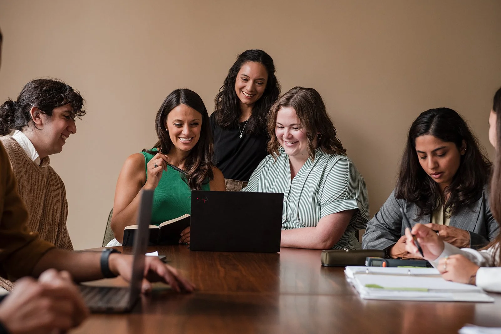 Group of people gathered around a table looking at a laptop and smiling.