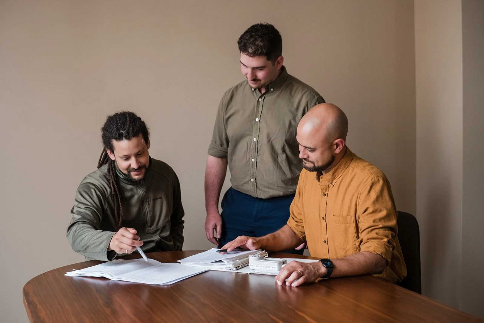 Three men collaborating around a table with papers and documents
