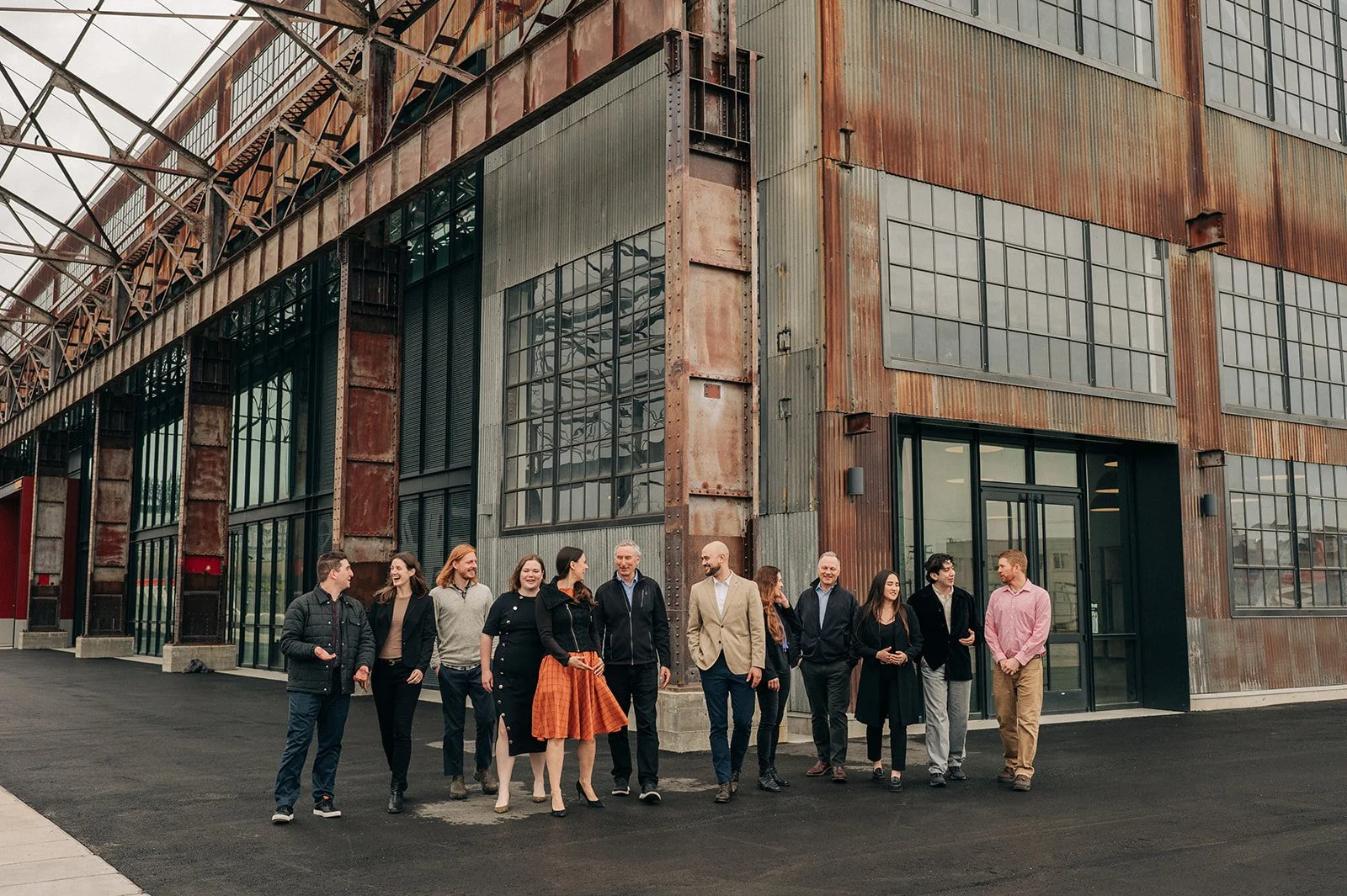 A group of ten people walking and talking outside a modern industrial-style building with large windows and rusted metal siding.