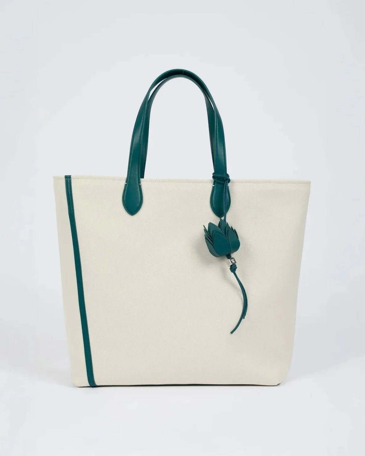 Cream-colored tote bag with teal handles and trim, and a decorative teal flower charm hanging from one handle.
