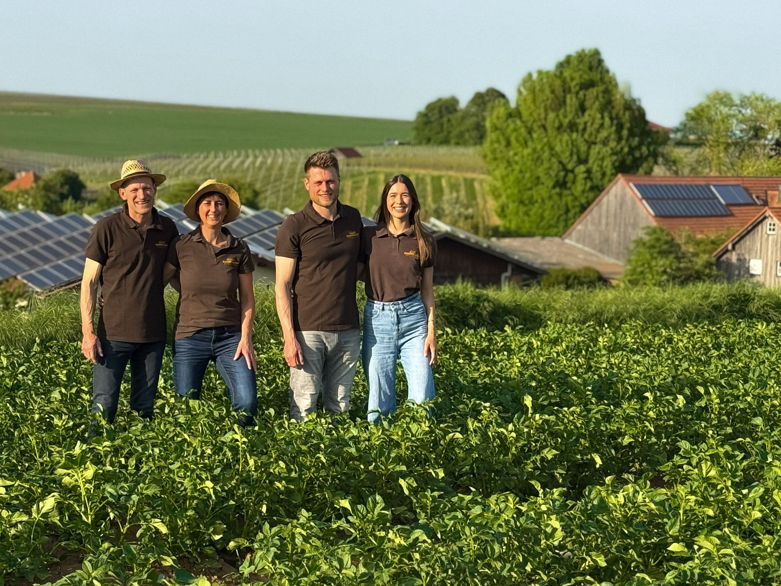 Familie Schäffer auf einem Familienbild im Kartoffelfeld mit dem Kartoffelhof Schäffer im Hintergrund
