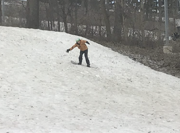 Person snowboarding on a snowy hill during winter, wearing a green helmet and orange jacket.