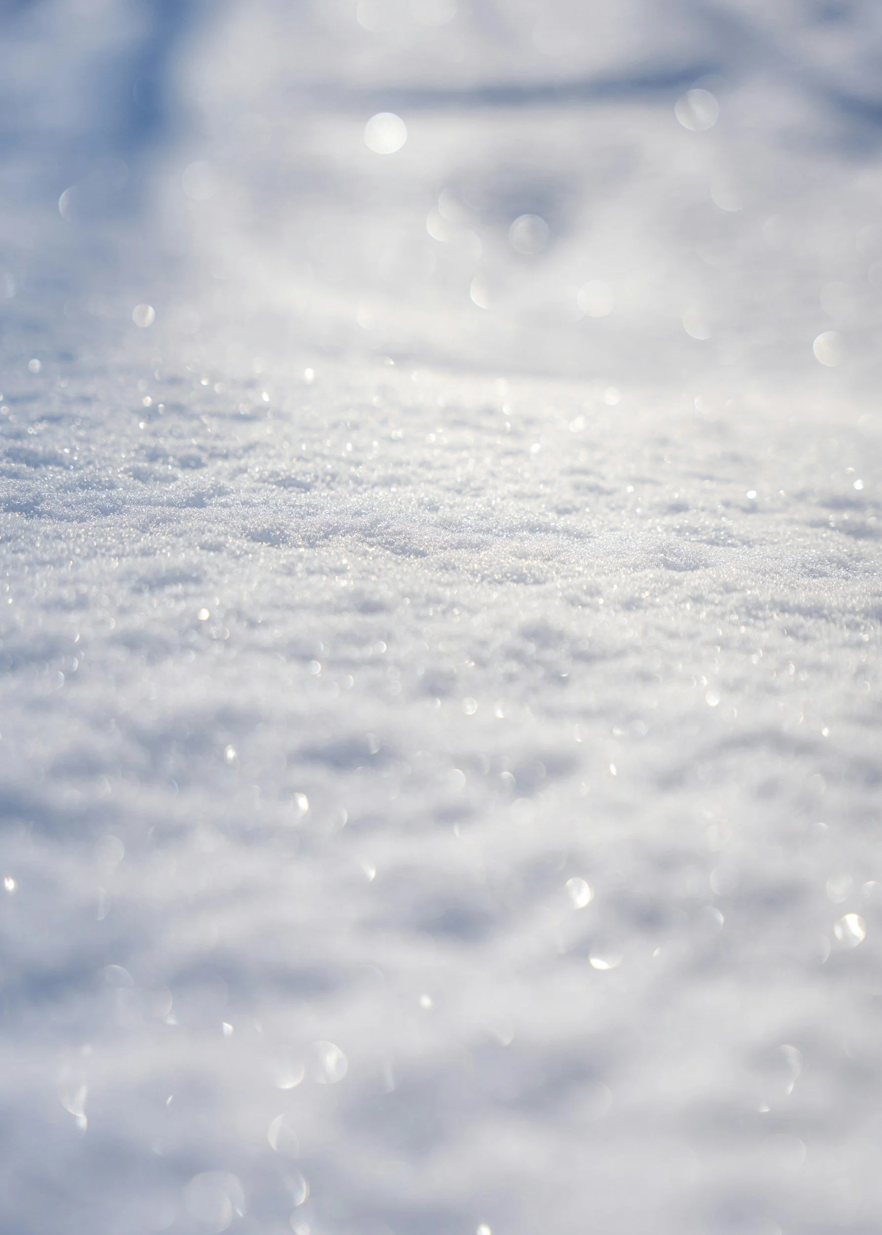 Close-up of snow-covered ground with sunlight reflecting off ice crystals, blurry background with bokeh effect.