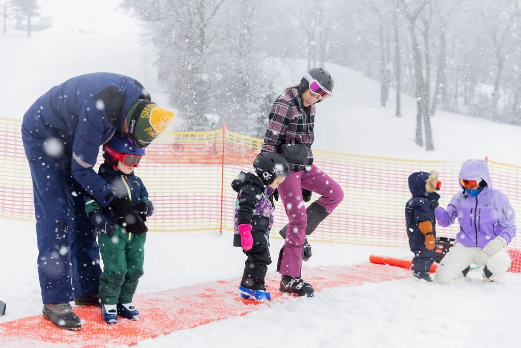 A snowboarding lesson with children and instructors on a snowy mountain, with safety gear and a bright snow background.