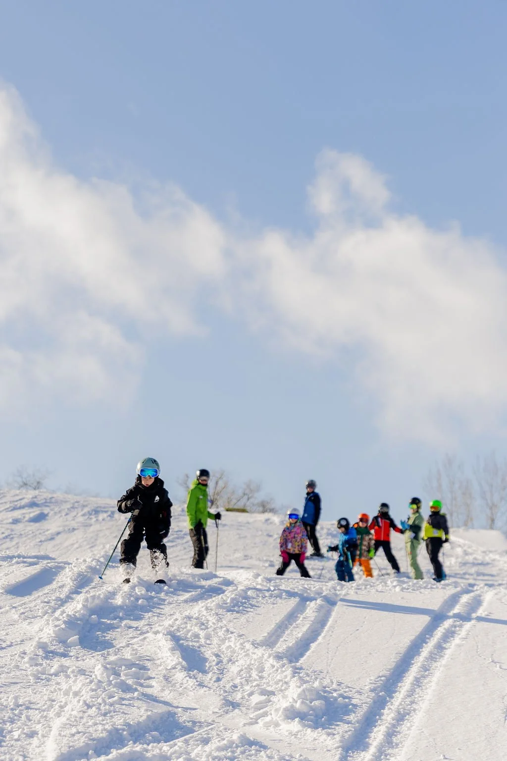 Group of children and adults skiing on snowy hill under cloudy sky.