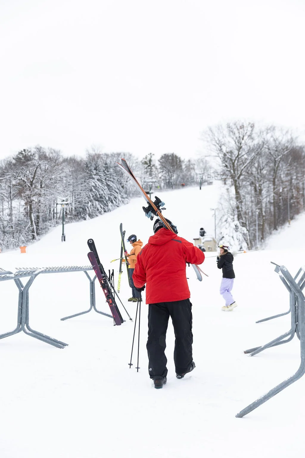 People at a ski resort, some wearing skiing gear, in a snowy mountain landscape with trees covered in snow.