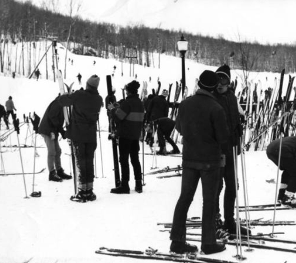 People standing on snow-covered ground with skis and ski equipment at a ski resort or mountain area.