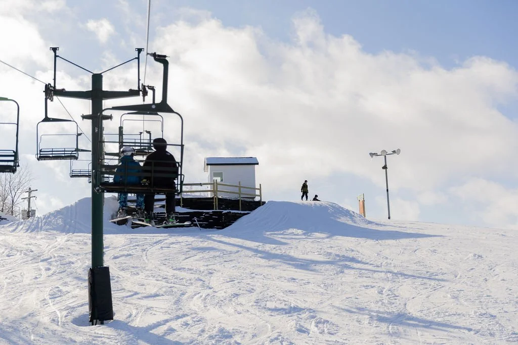 People riding a ski lift at a snowy ski resort during the day with cloudy sky.