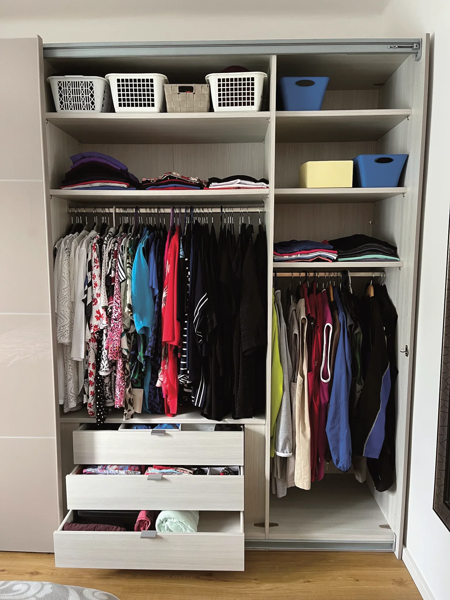Ein offener Kleiderschrank mit mehreren Regalen, in denen Kleidung und Accessoires ordentlich aufbewahrt werden.