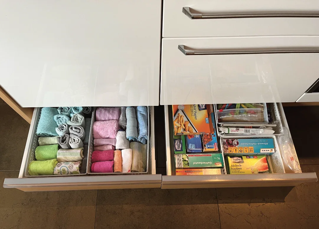 Offene Küchenschublade mit handtuchartigen Socken, in einer Hälfte. In der anderen Hälfte befinden sich Brettspiele, Papiere und Bastelmaterial in einer Schublade.