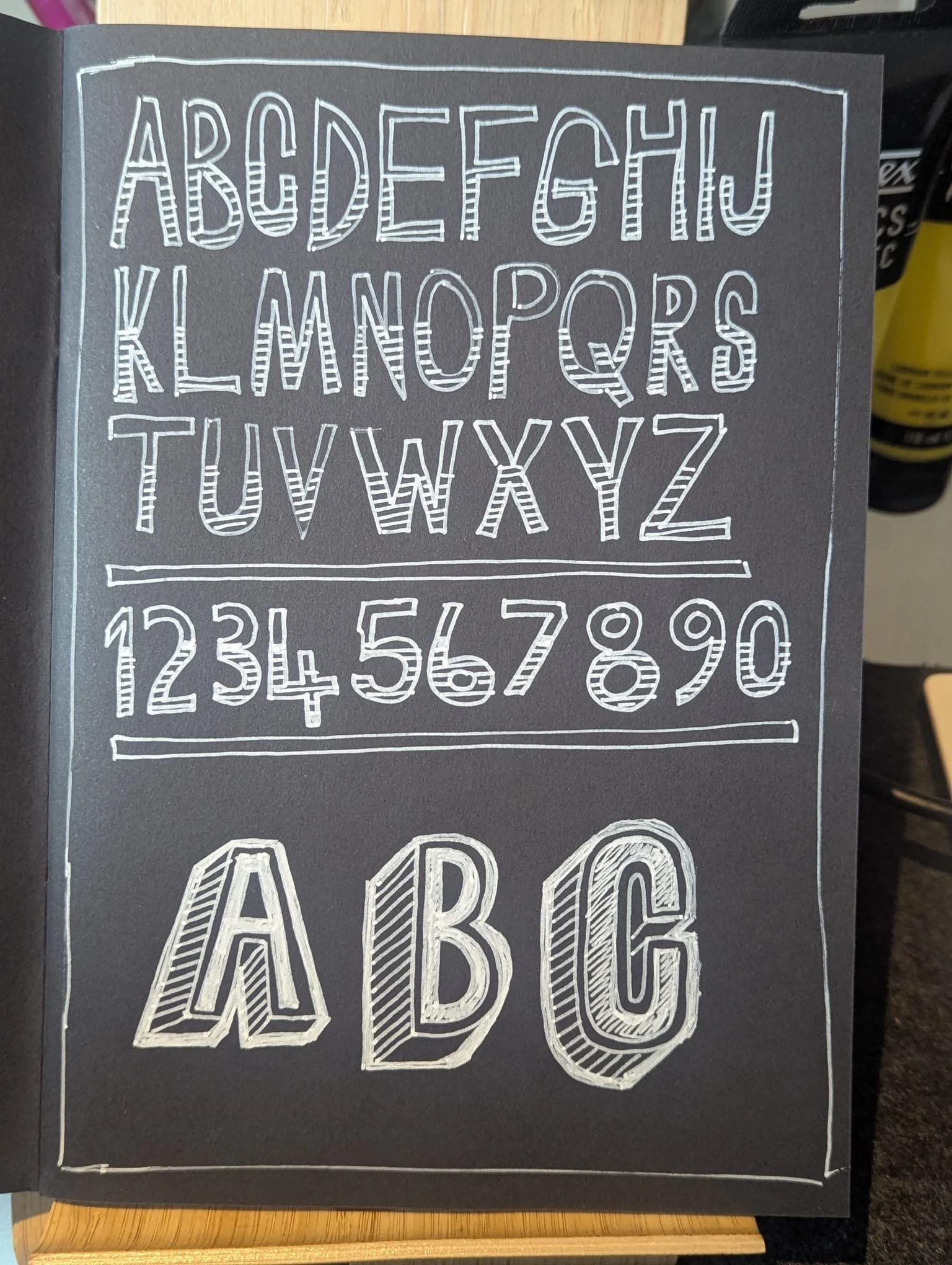 Black chalkboard with white handwritten alphabet letters and numbers, displayed in bold, decorative styles.