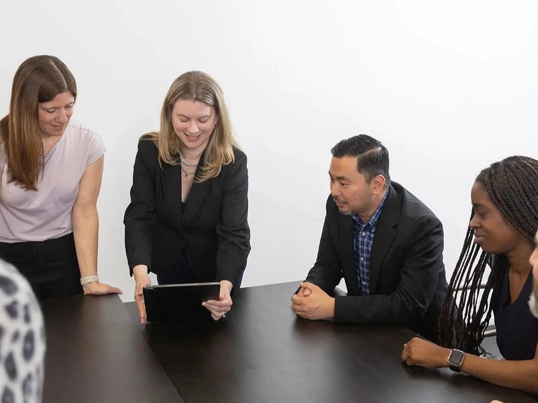 Group of five people in a business meeting, looking at a tablet device.