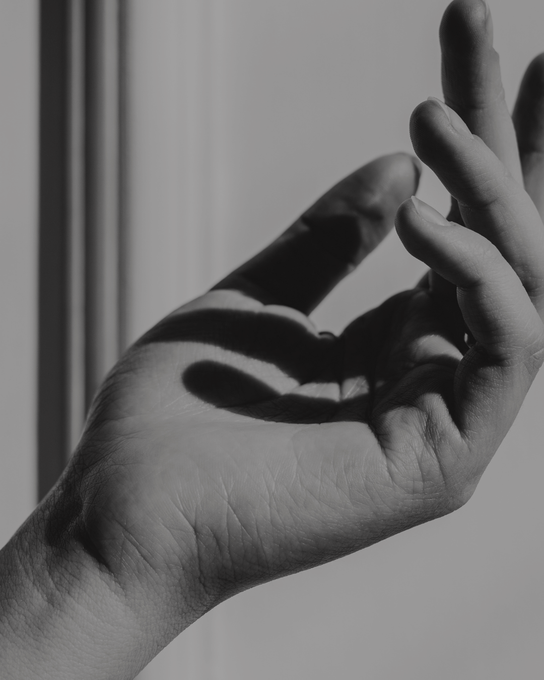 Close-up black and white photo of a hand with fingers slightly bent, casting shadows on the palm and fingers.