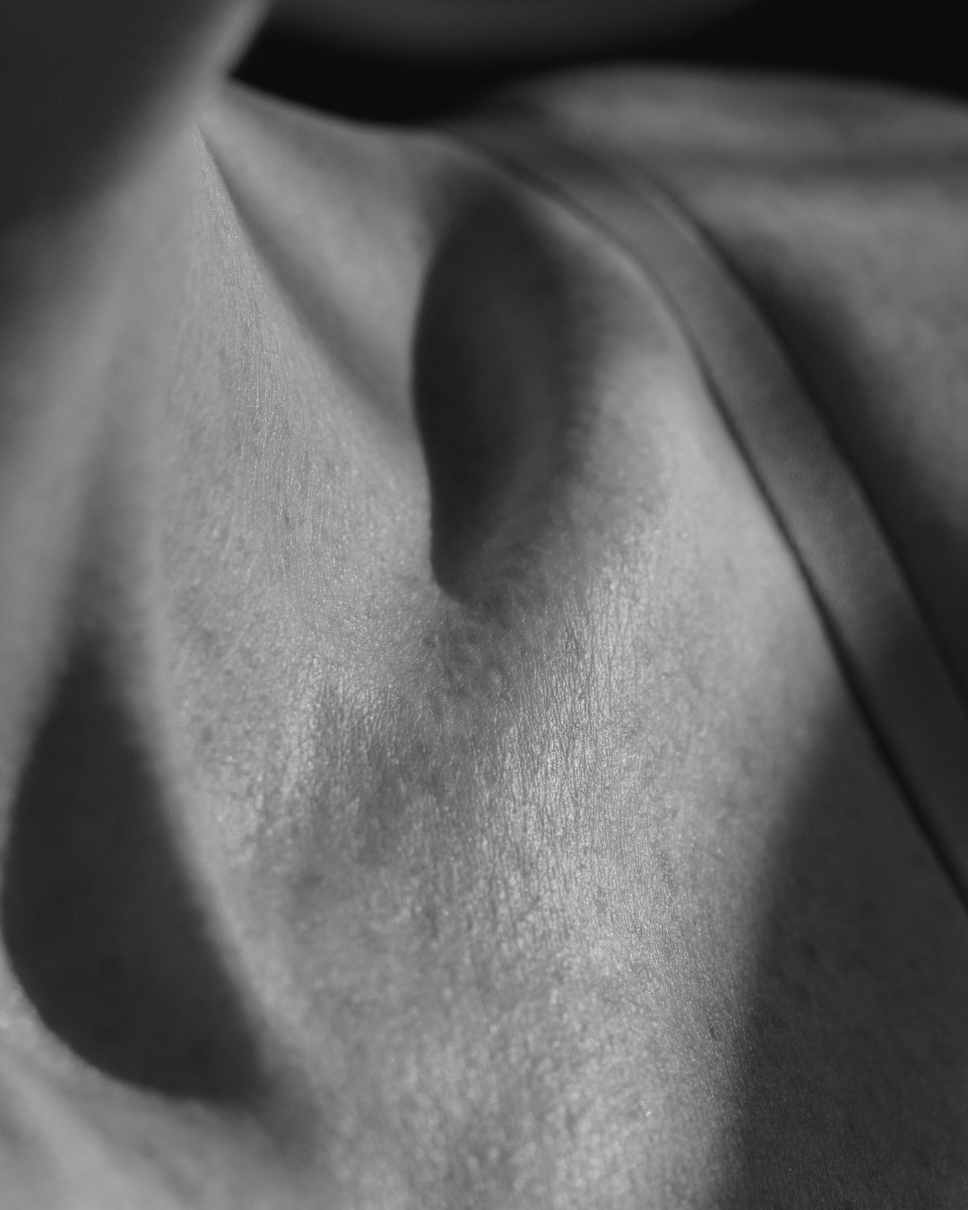 Close-up black and white photograph of a person's bare shoulder and collarbone area, showing skin texture and shadows.