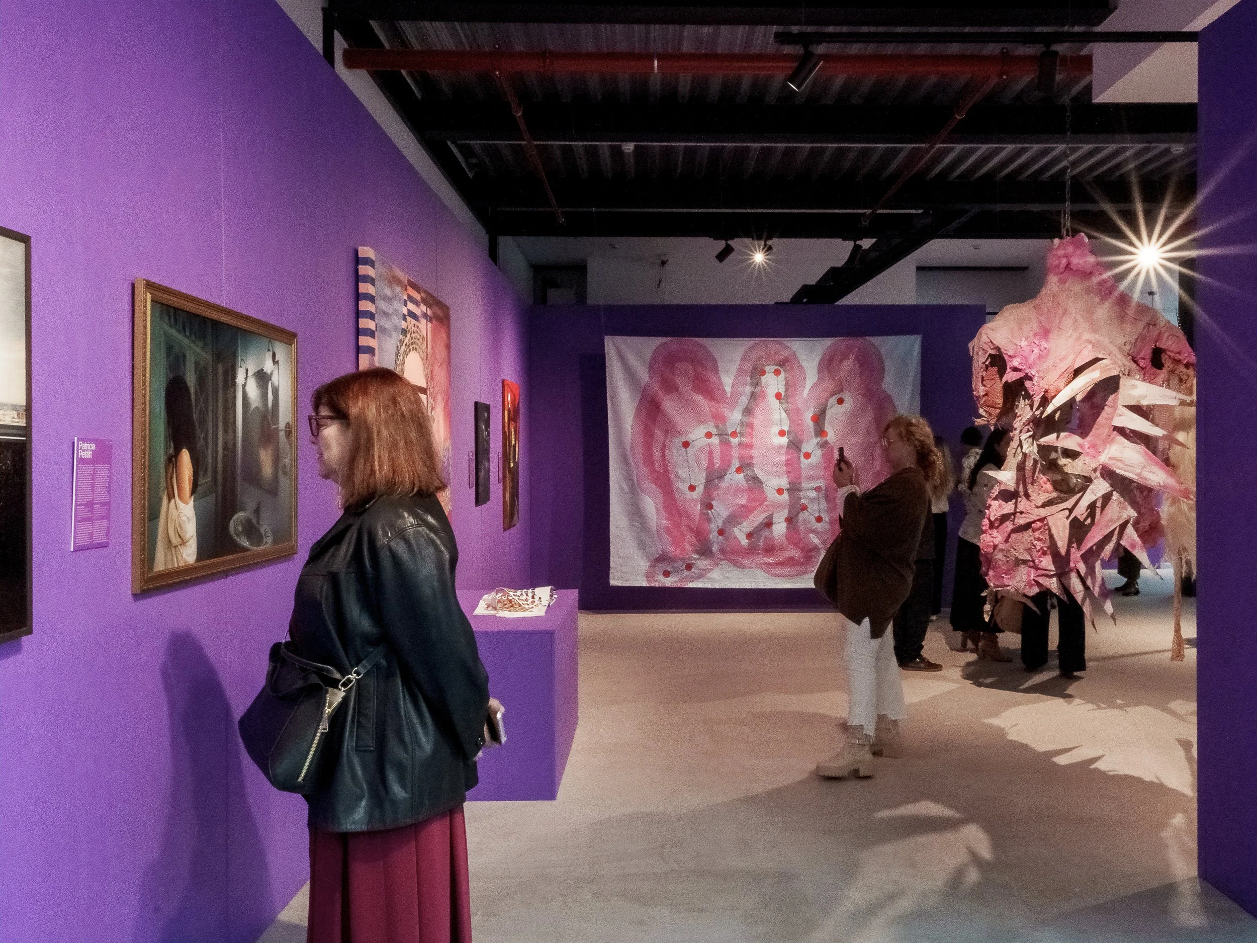 Pessoas observando obras de arte em uma galeria de arte com paredes roxas.