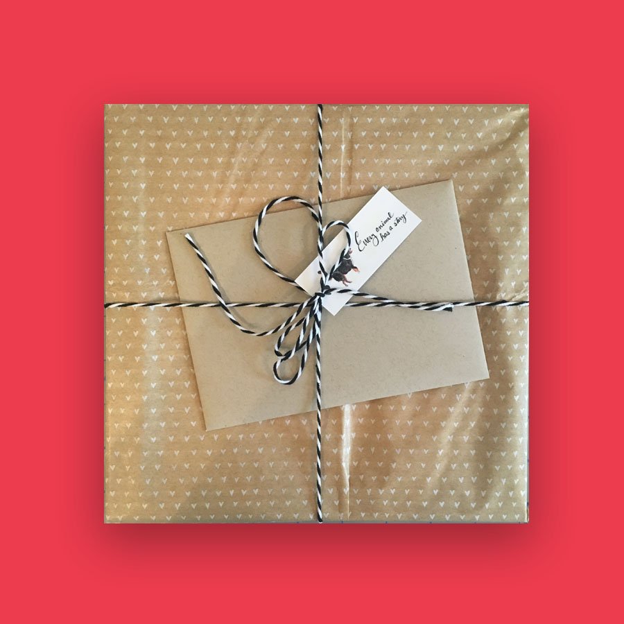 A wrapped gift box with black and white string bow, a gift tag, and beige wrapping paper with small white hearts on a red background.
