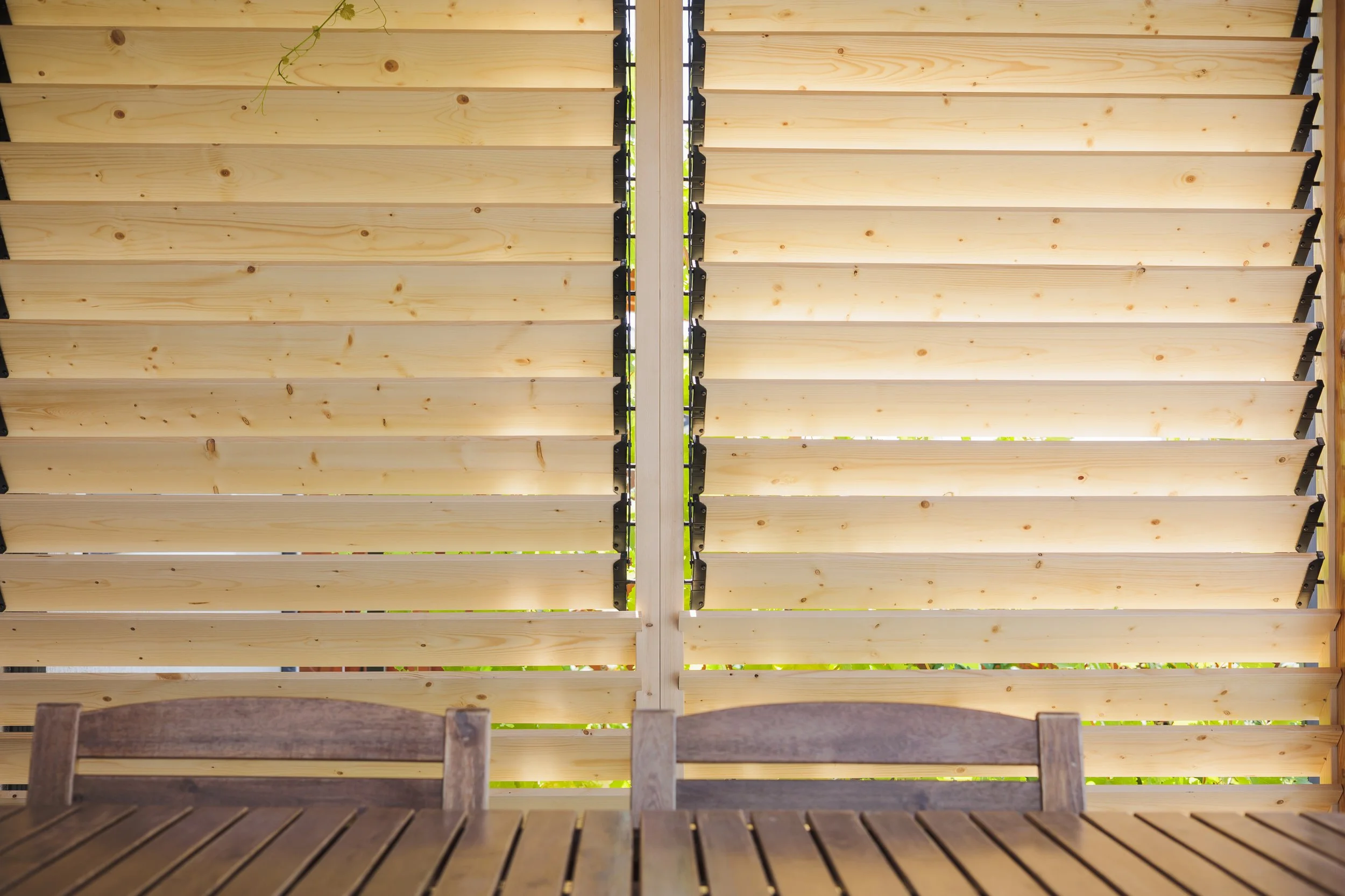 Wooden slats forming a ceiling or roof with black brackets, viewed from below with a wooden bench in the foreground.