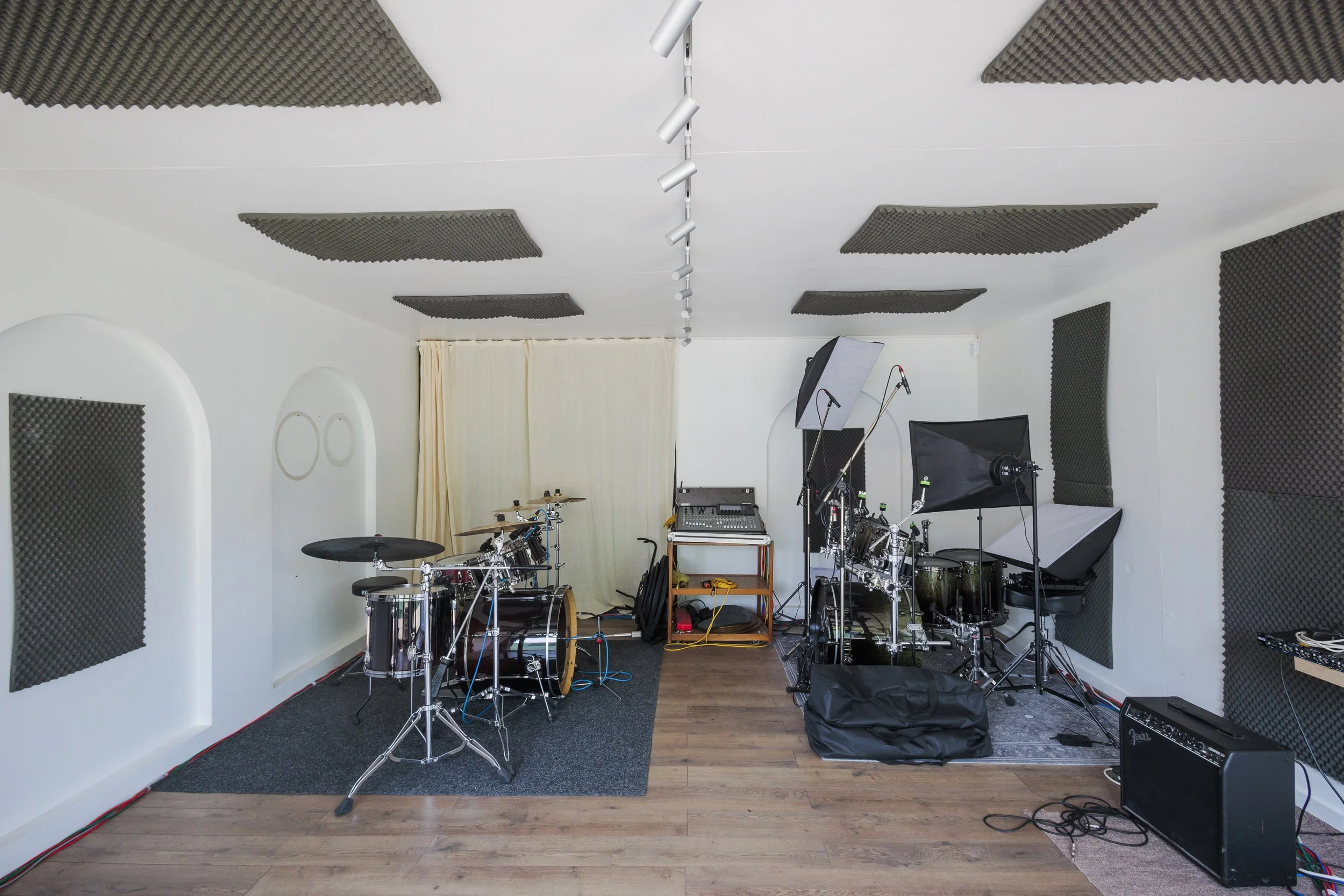 A music rehearsal or recording studio with drums, microphones, soundproofing panels on the walls, and various audio equipment.