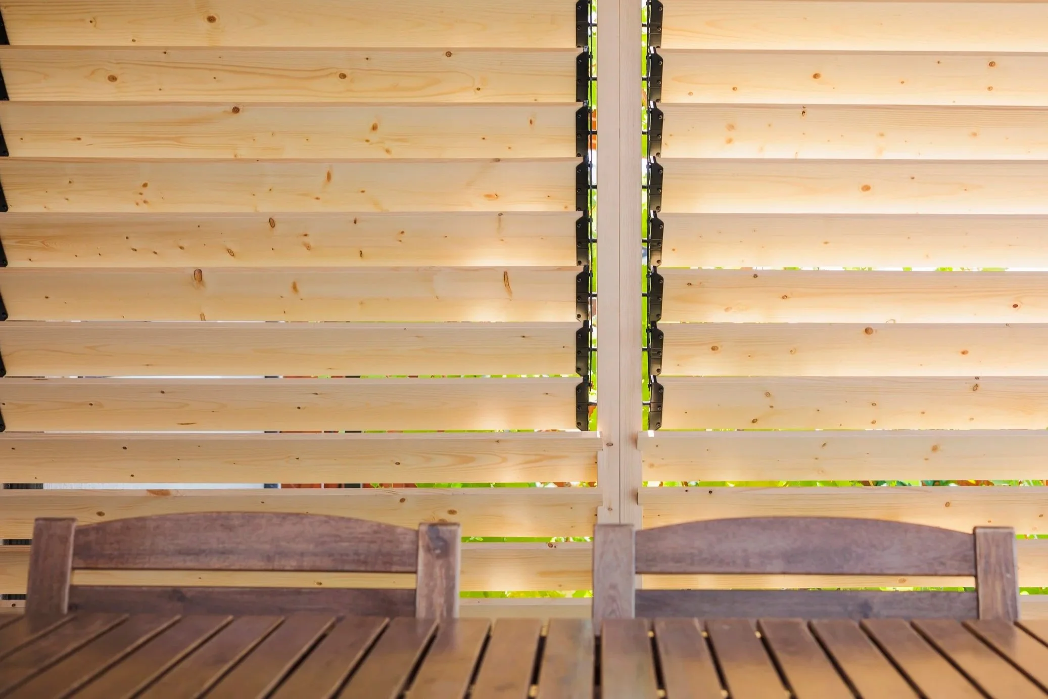 Wooden slatted outdoor pergola or roof structure with black brackets and support beams, viewed from below.