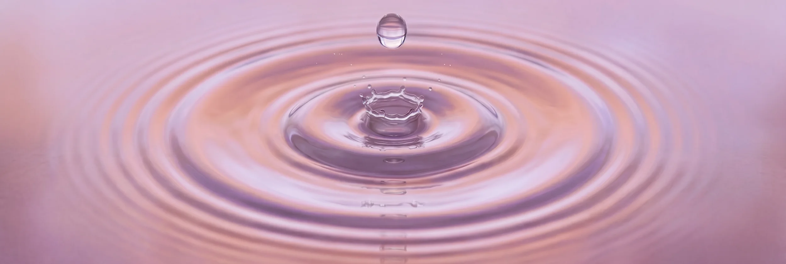 Une goutte d'eau tombe dans une surface d'eau, créant un cercle de vagues concentriques avec une petite couronne d'eau au centre.
